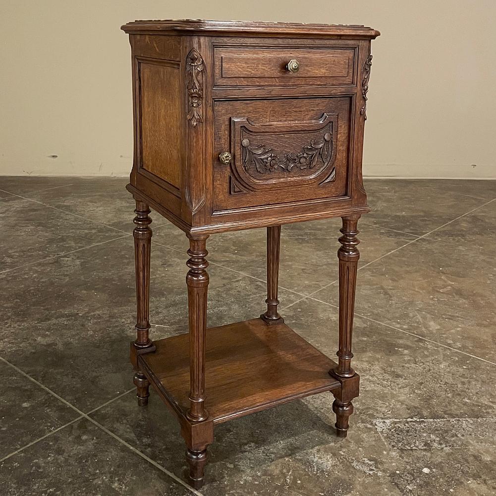 19th century Country French Louis XVI marble top nightstand was hand-crafted and hand-carved from solid oak, and features a luxurious Griotte marble top for carefree luxury. Carved floral garlands appear the door, with florals on the cornerposts as