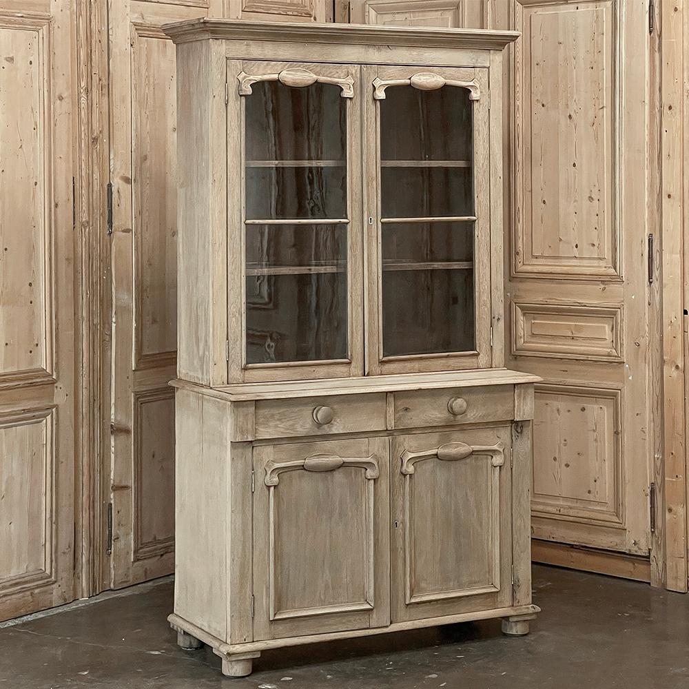 19th Century Country French Neoclassical Bookcase in Stripped Oak features architectural lines inspired by the ancient masters with a touch of decorative ornamentation surrounding the glass above and door panels below that hints at the beginnings of