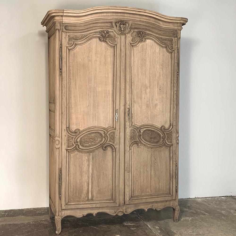 19th century country French Normandy stripped oak armoire features the graceful lines that characterize the breed, with an elegant chapeau de gendarme cornice appearing on top, overlooking the finely carved bonnet and exquisitely carved tilted oval