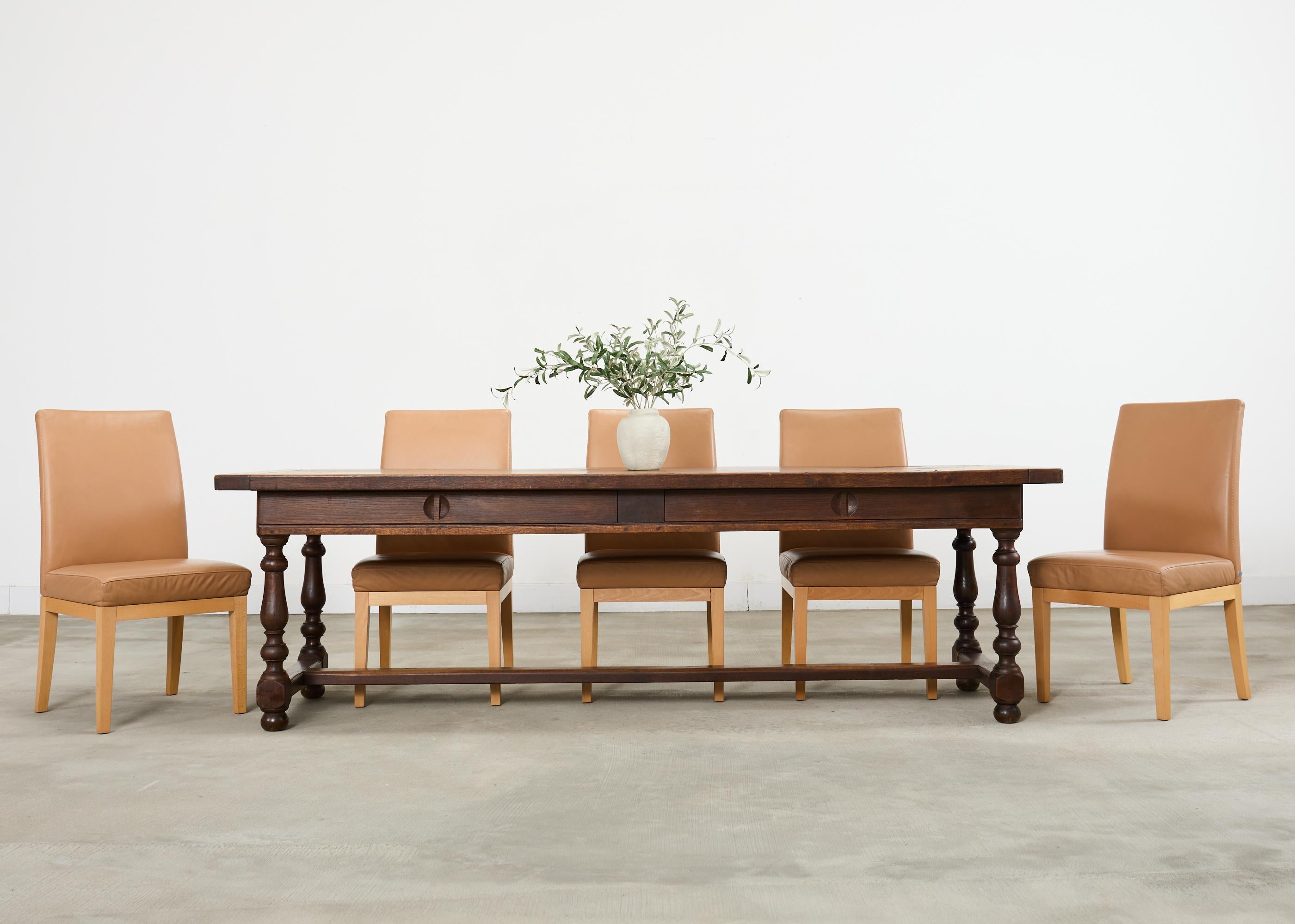 Imposing late 19th century country French provincial style farmhouse harvest dining table crafted from solid oak. The grand table features a thick oak plank top with breadboard ends. The top is supported by a long trestle base with sliding storage