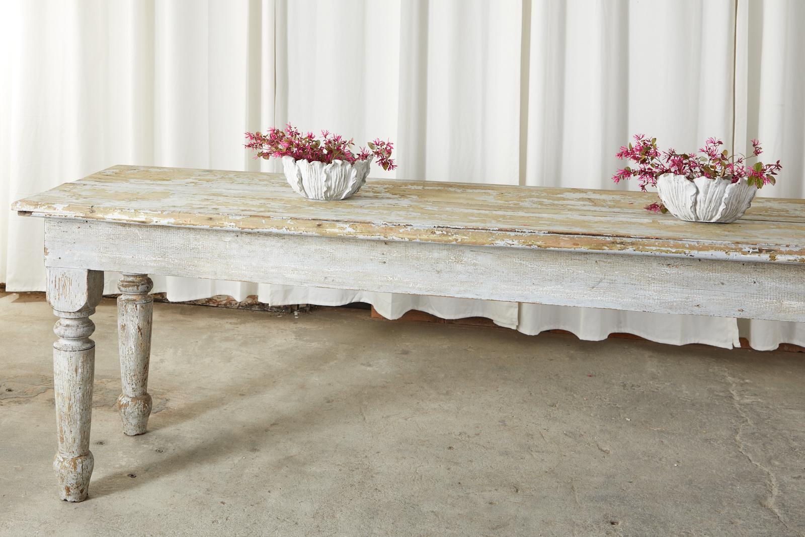 Massive late 19th century French farmhouse harvest table constructed from pine. The large scale table features a beautiful aged, distressed painted finish. At nearly 12 feet long this table is a very versatile piece with a plank top measuring 34