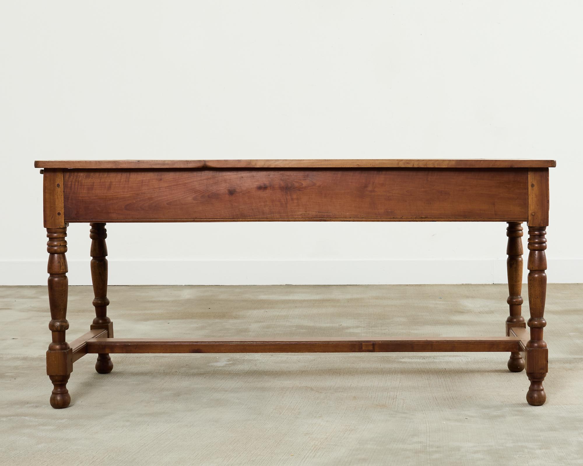 Gorgeous late 19th century country French provincial farmhouse work table or dining table crafted from fruitwood. The table features a framed plank top supported by a trestle base. The work table has a storage drawer on one end with an iron ring
