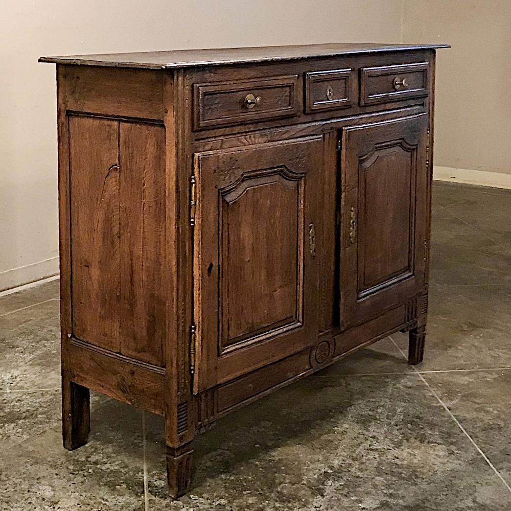 19th century Country French Provincial oak buffet represents the classic interpretation of the style, with subtly scrolled framework around the recessed door panels, and a trio of drawers fitted with brass pulls, and brass keyguards on the cutlery