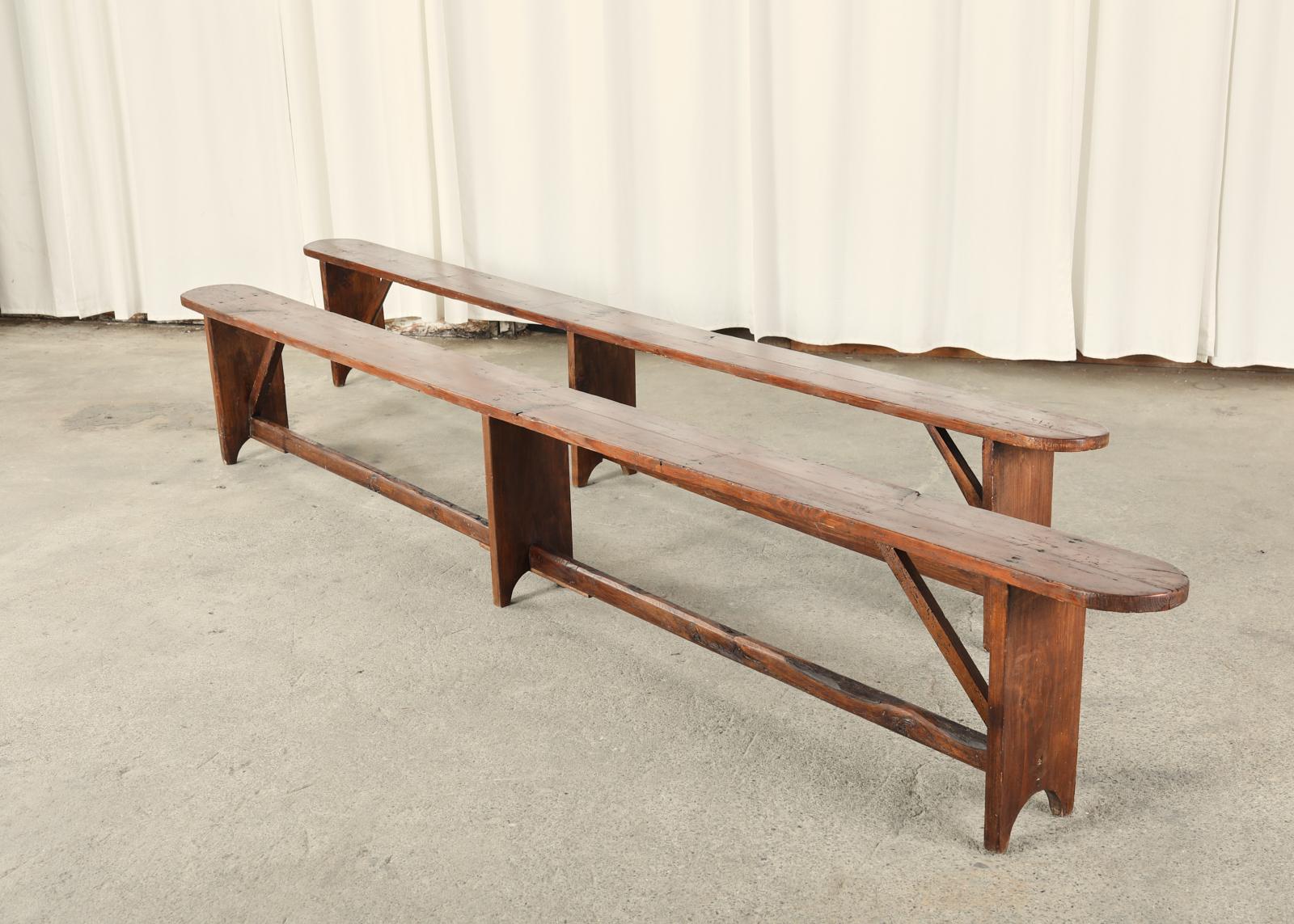 Monumental pair of 19th century country French provincial farmhouse harvest benches crafted from pine. These rustic benches are over 10 feet long and feature long pine planks measuring 1 inch thick. The trestle style base has three legs conjoined by