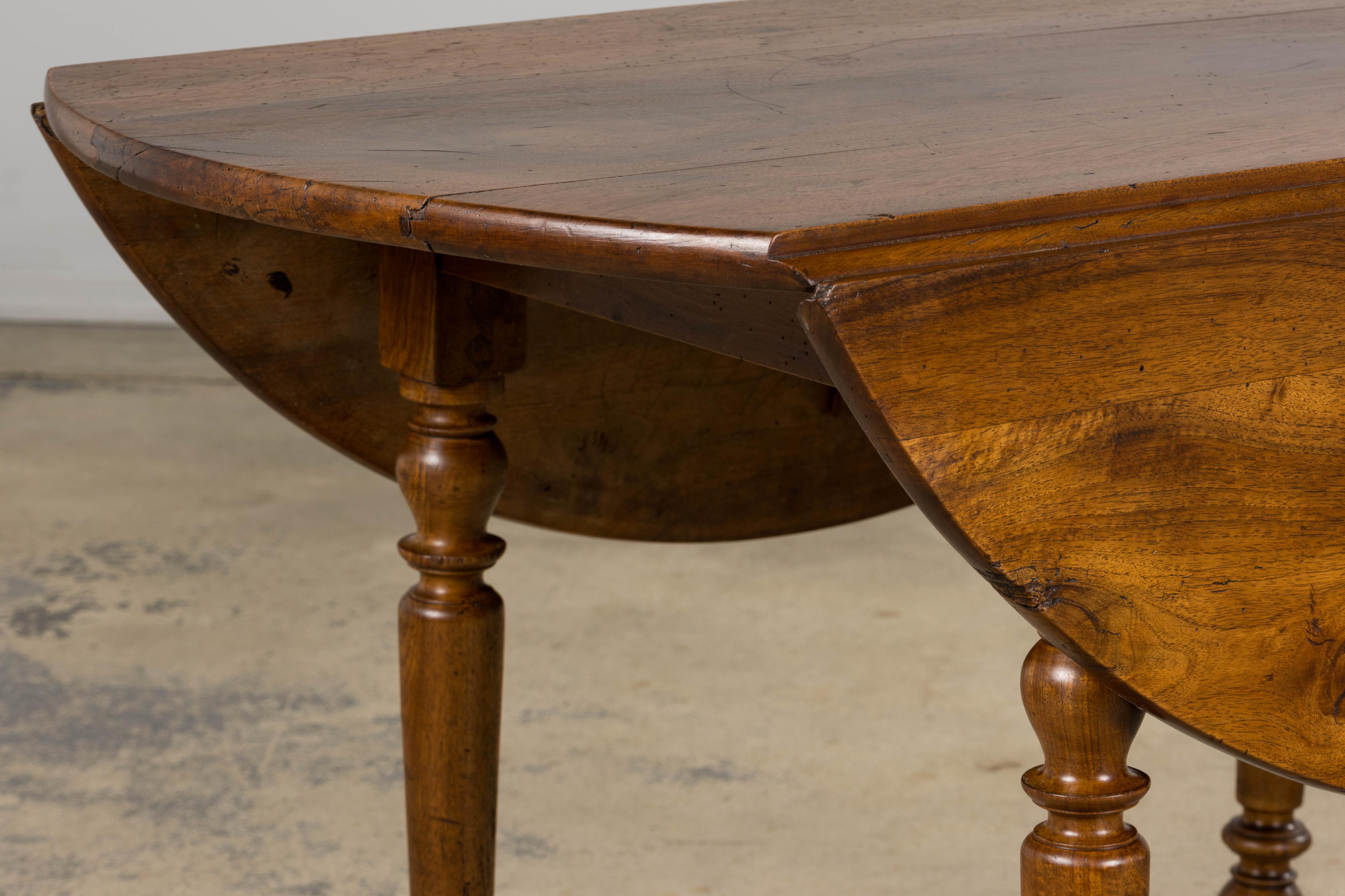 A refined 19th-century French Provincial drop-leaf table, handcrafted from solid walnut and sourced in Provence, France. The circular top is finished in a warm medium-brown tone that highlights the expressive grain patterns and naturally aged patina