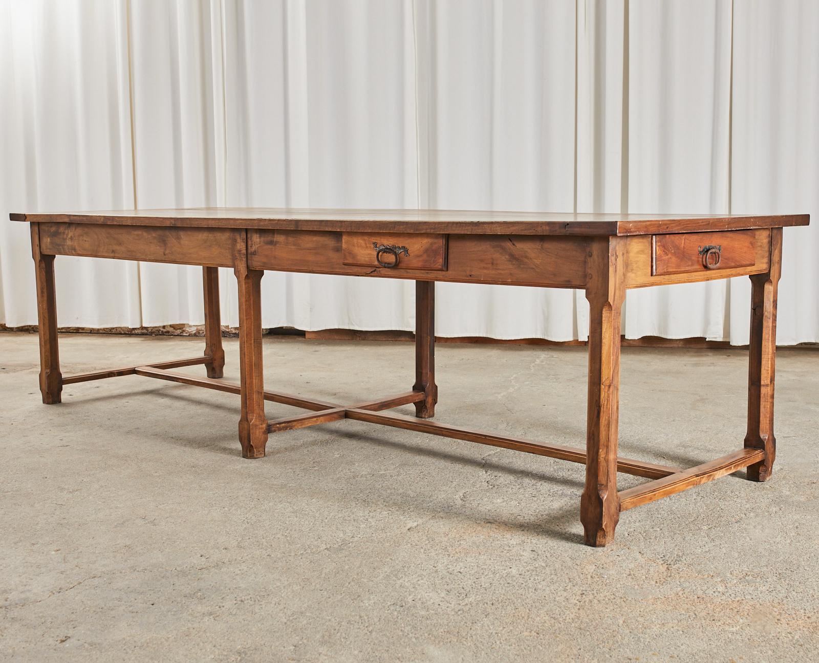 Monumental 19th century country French provincial farmhouse trestle dining table or refectory table hand-crafted from walnut. The massive table has a 1.25 inch thick plank top with breadboard ends. All four sides of the table have a storage drawer