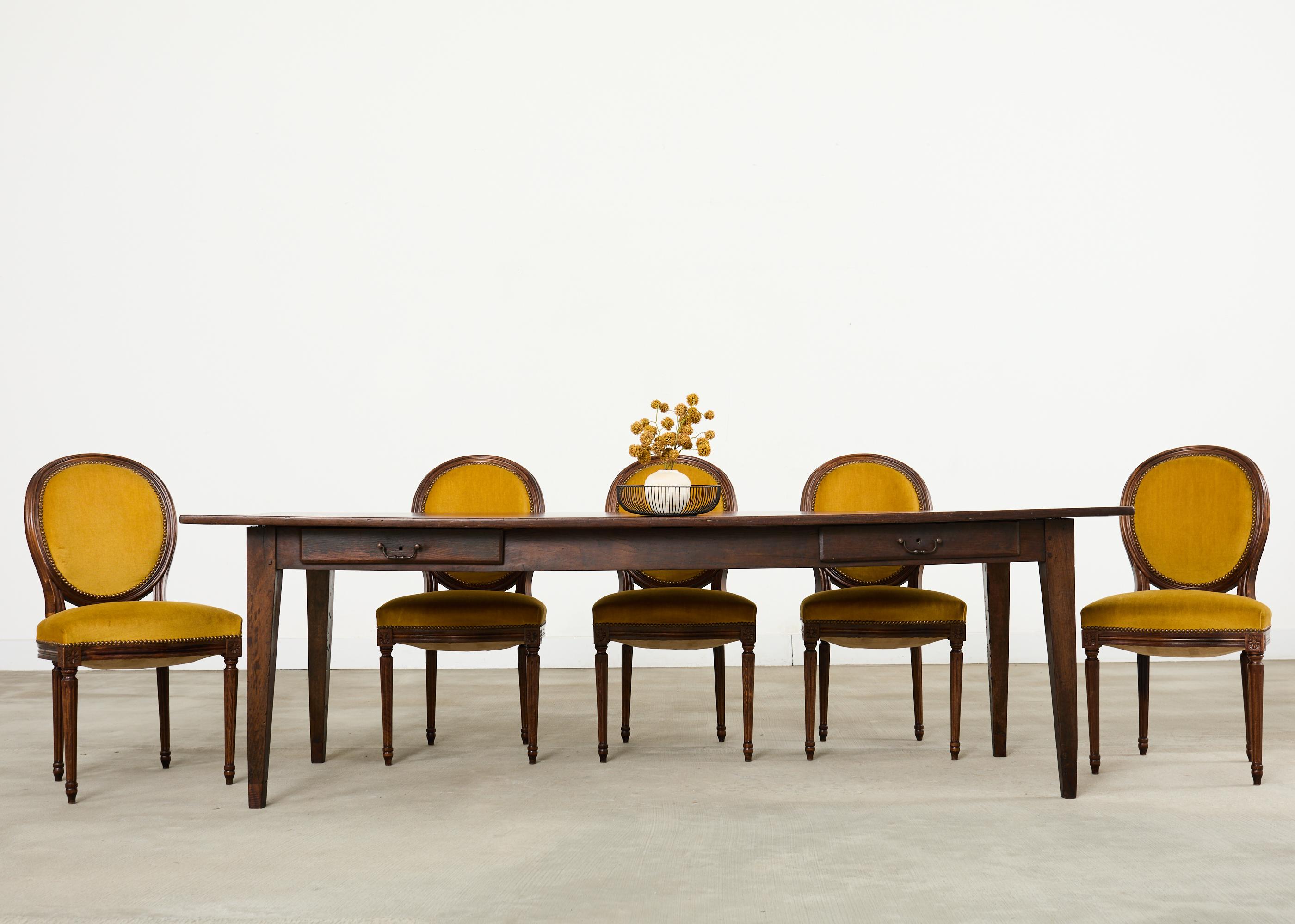 Quintessential 19th century country French provincial farmhouse dining table crafted from rich walnut. The table measures over 7.5 feet long and features a thick plank top. The front of the apron is fitted with two storage drawers with patinated