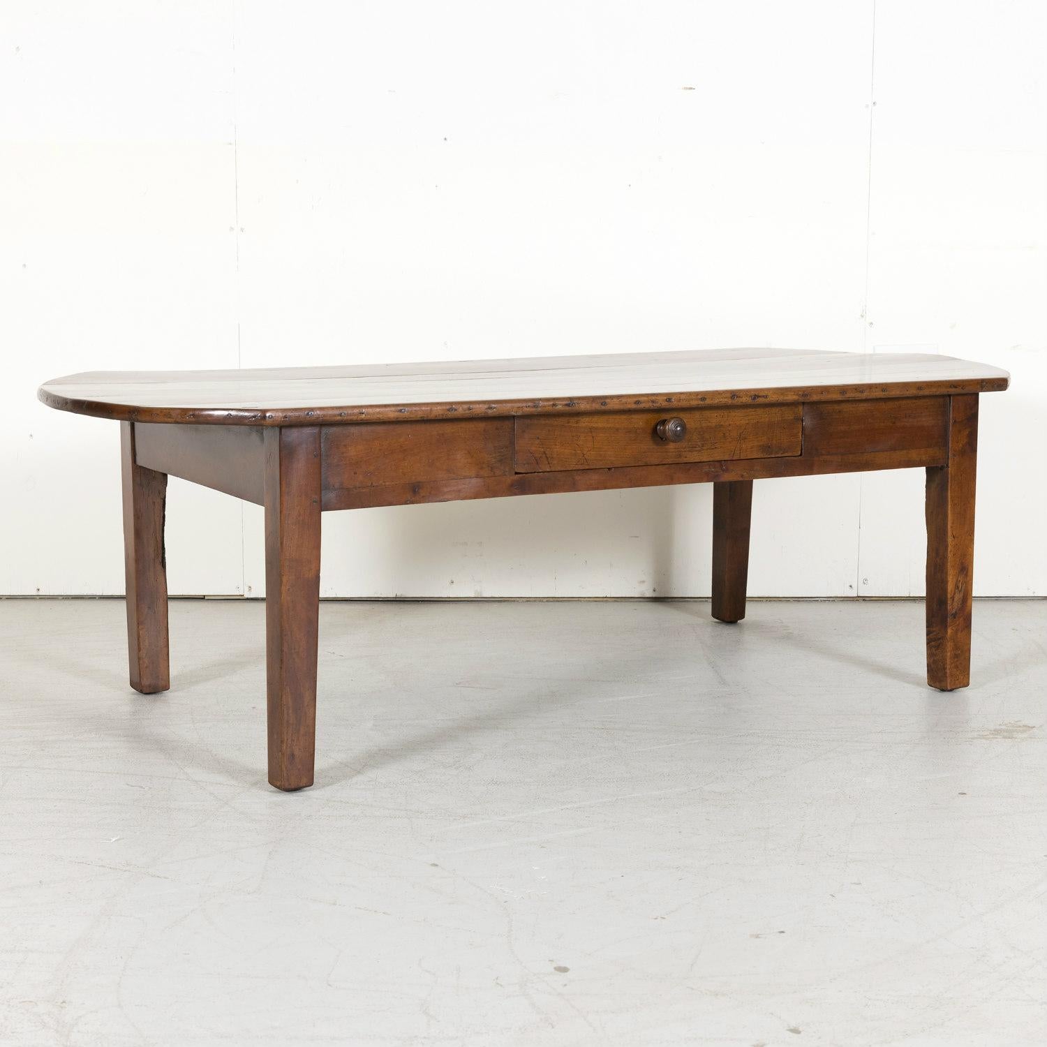 A large 19th century Country French coffee table handcrafted of solid cherry in Normandy, having a wide oval plank top over a single apron drawer, circa 1870s. Raised on square, tapered legs.This rustic, provincial coffee table has a wonderful color