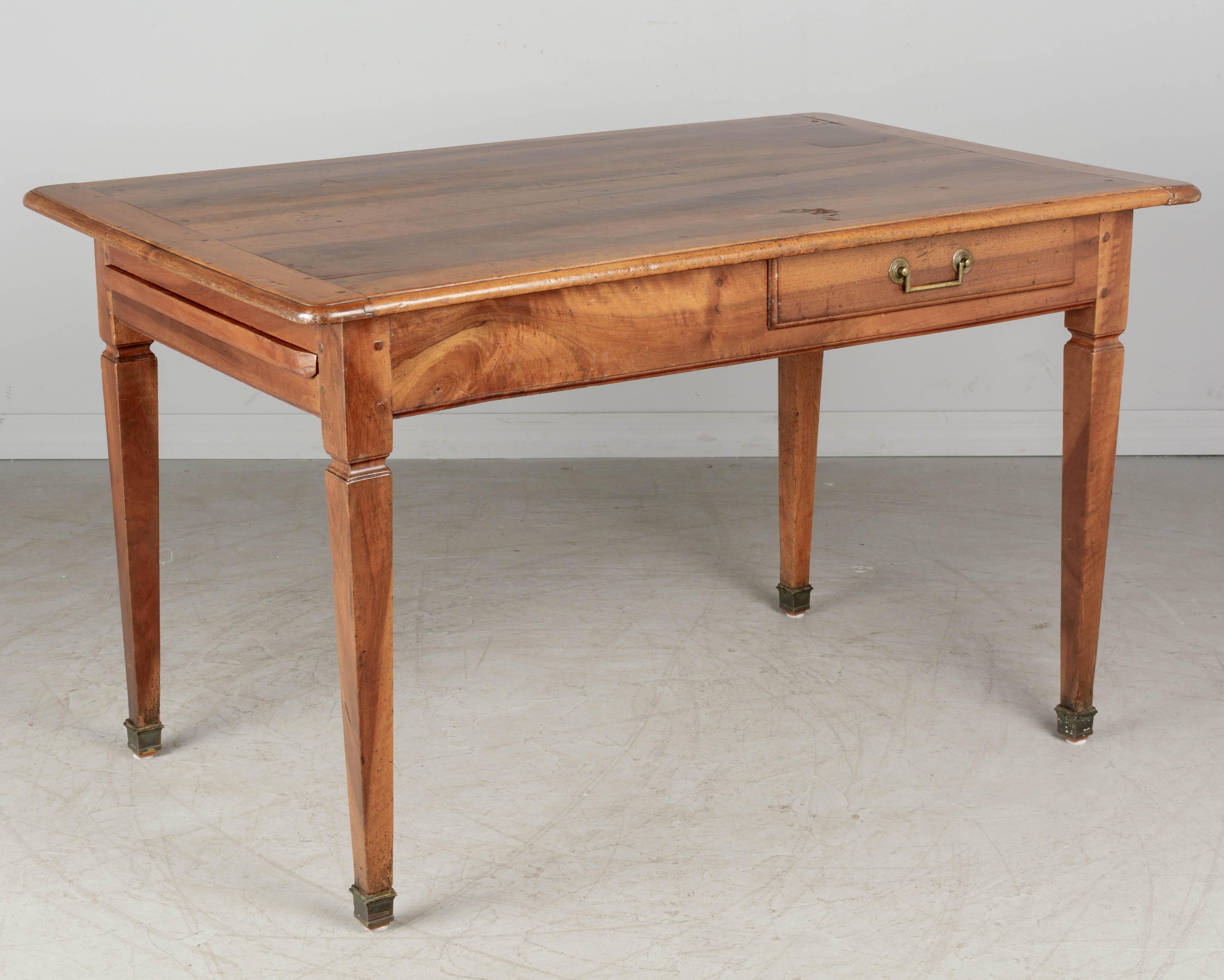 An early 19th century Louis XVI style Country French farm table made of solid walnut. Top is made from three planks with nice wood grain and rounded corners. Dovetailed drawer for silverware with divided interior and brass pull. Pull-out cutting