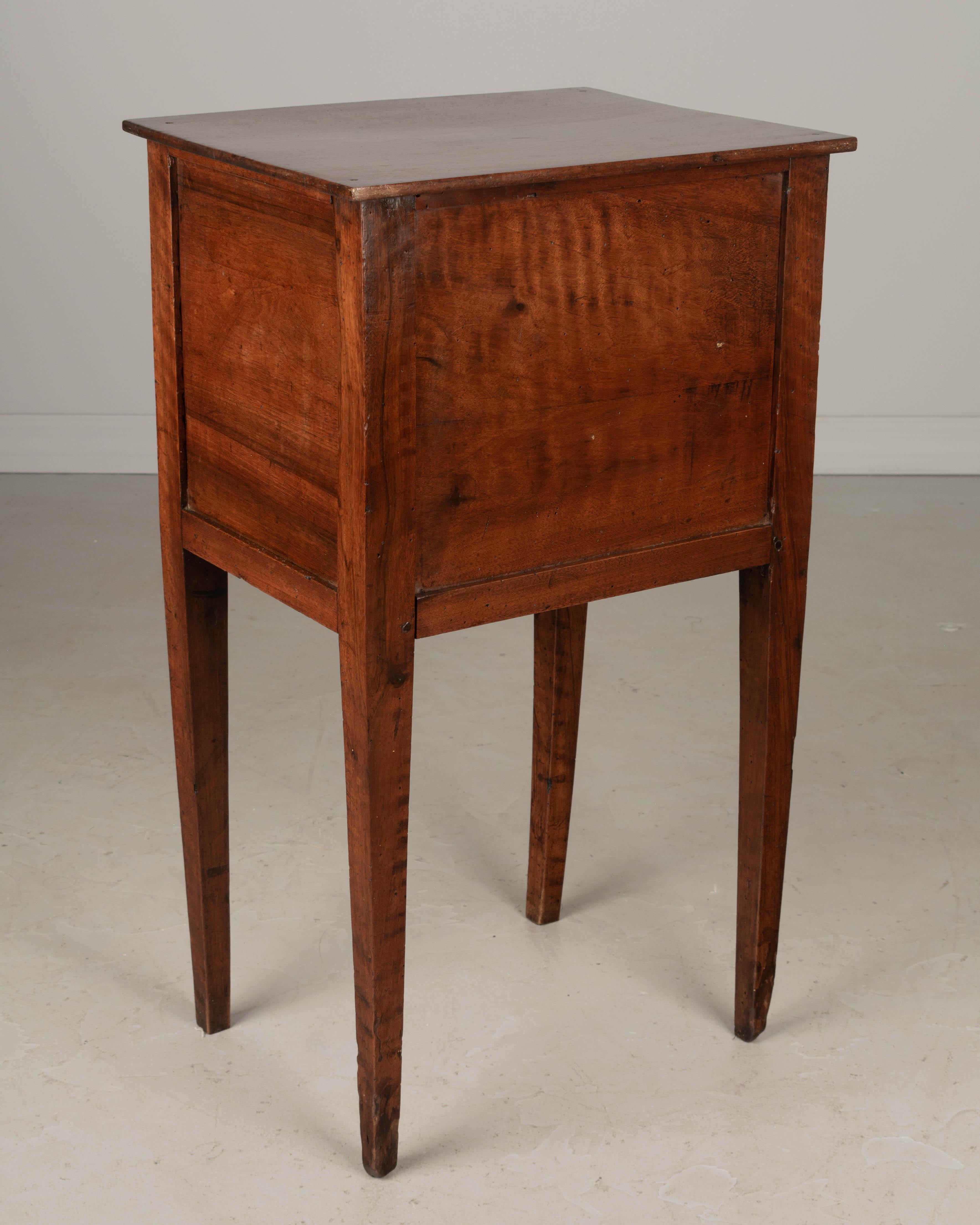 An early 19th century Country French side table, handcrafted of solid walnut and finished on all four sides. Three dovetailed drawers with mahogany face, two with working locks and one key. One brass knob is not matching. Sturdy tapered legs. Pegged