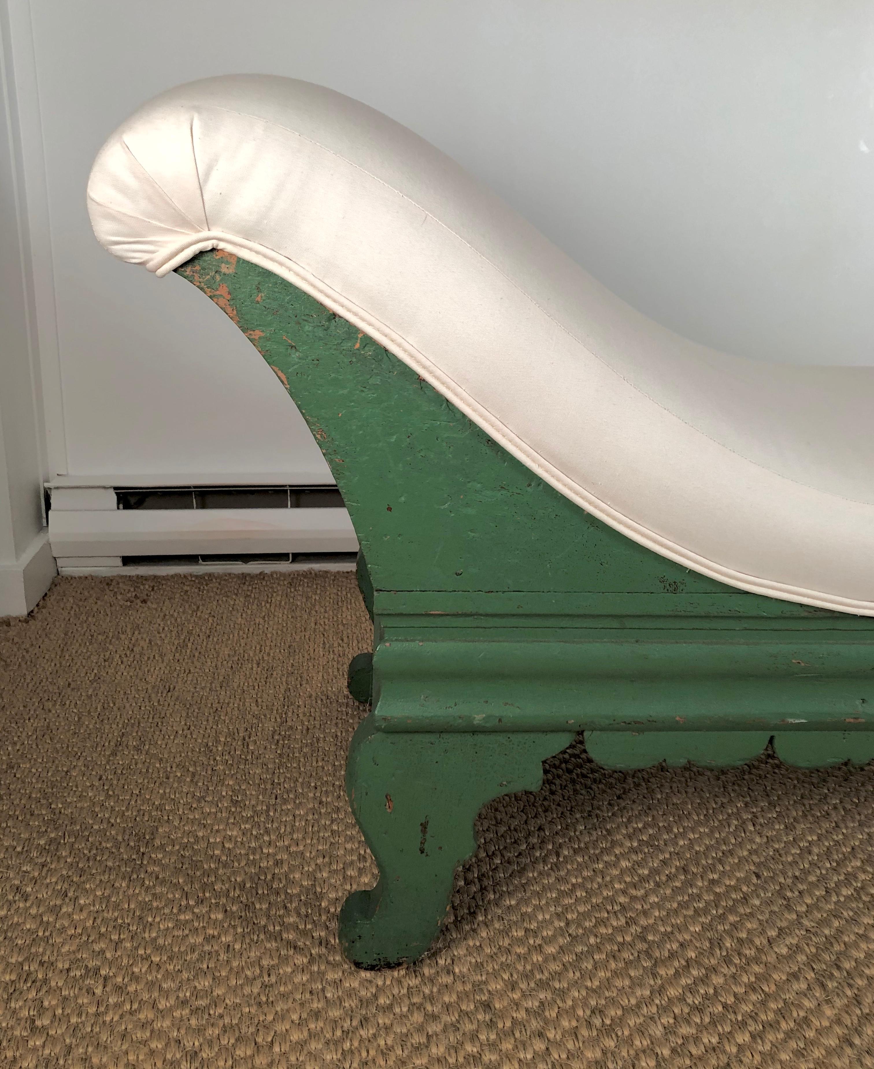 A 19th century American Country green painted and carved wood chaise longue, upholstered in white duck cloth, the frame with carved bracketed decoration along the front edge, with a gently sloped back, and supported by four scrolled feet. Solid and