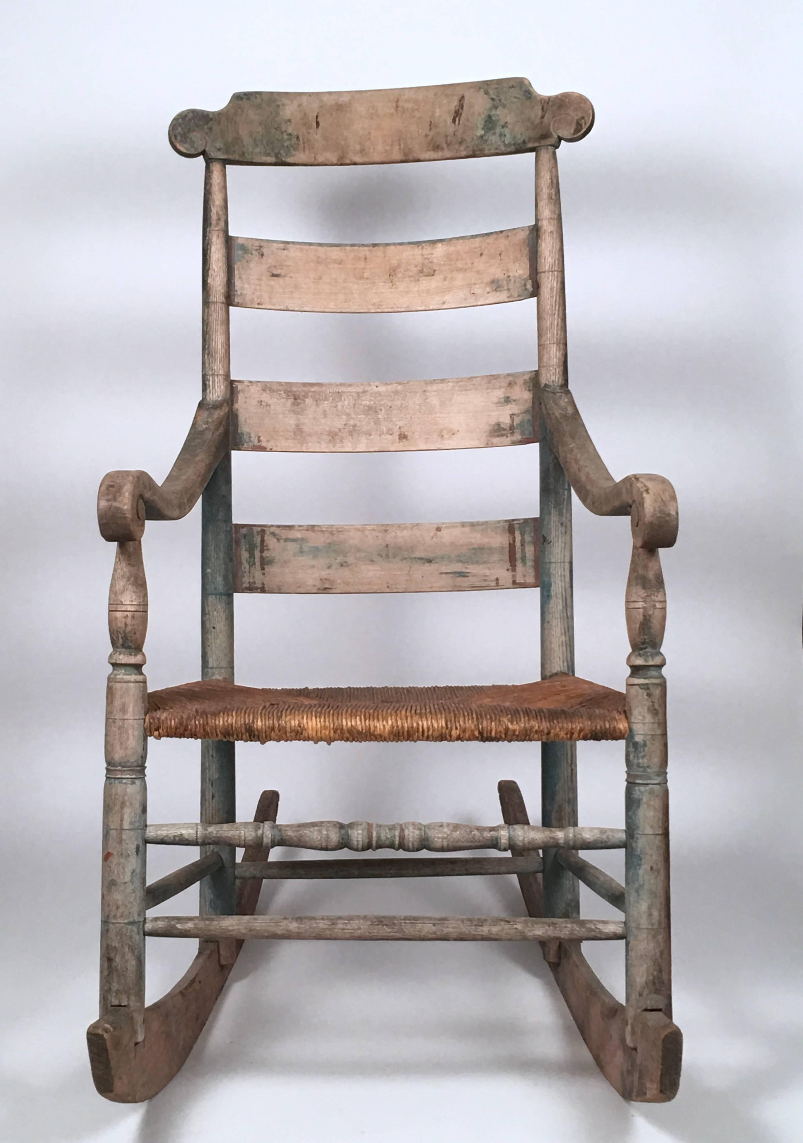 A very comfortable, 19th century high back rocking chair, retaining traces of its old blue painted surface, from Northern New England, or possibly Canada, the rectangular top rail with scrolled ends, over three curved ladder back supports, some