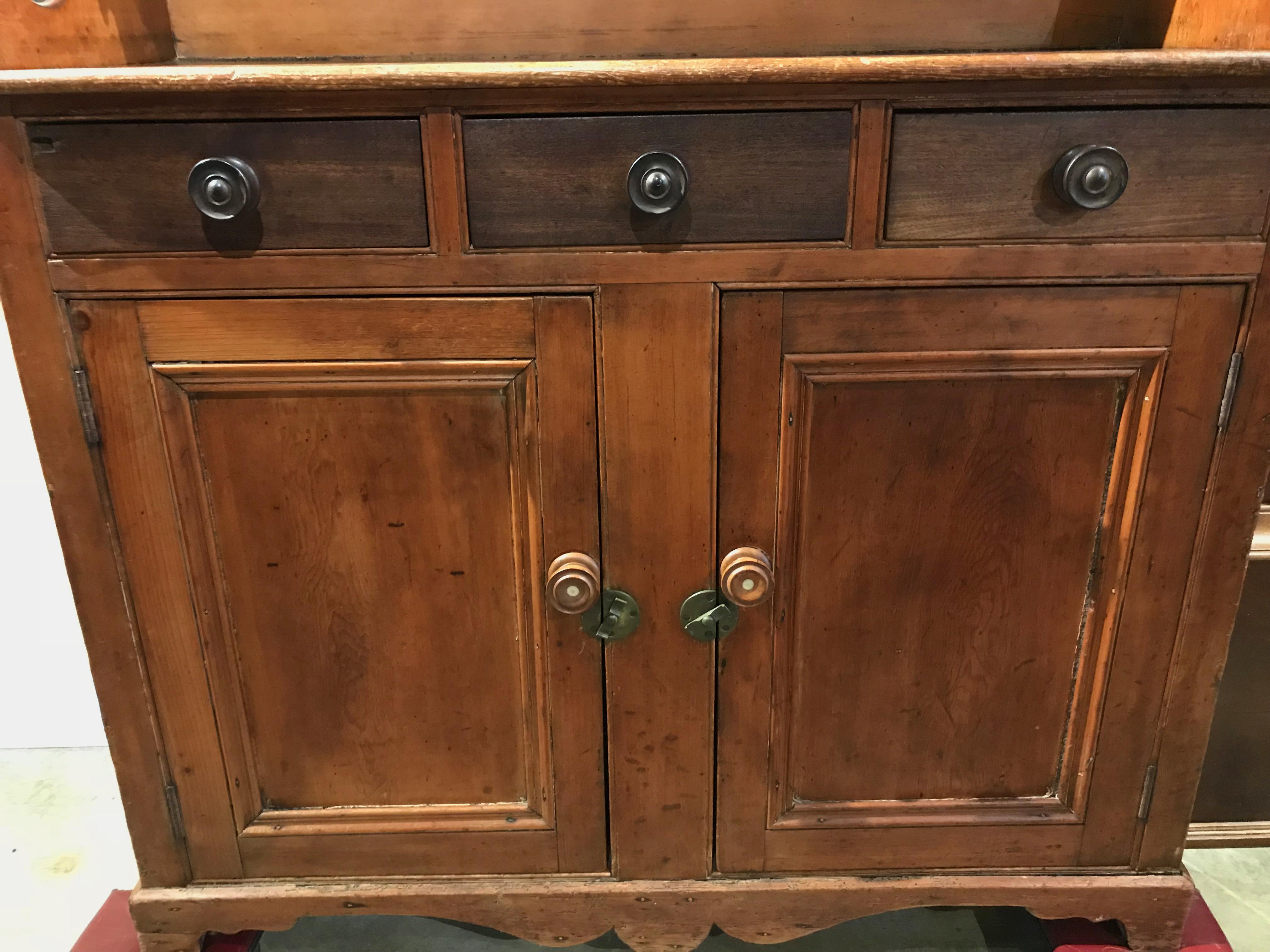 A wonderful form country step back cupboard or server, possibly Canadian in origin, with shaped crest, an upper shelf with five fitted small drawers, the lower case featuring three fitted frieze drawers over two paneled doors, which open to reveal a