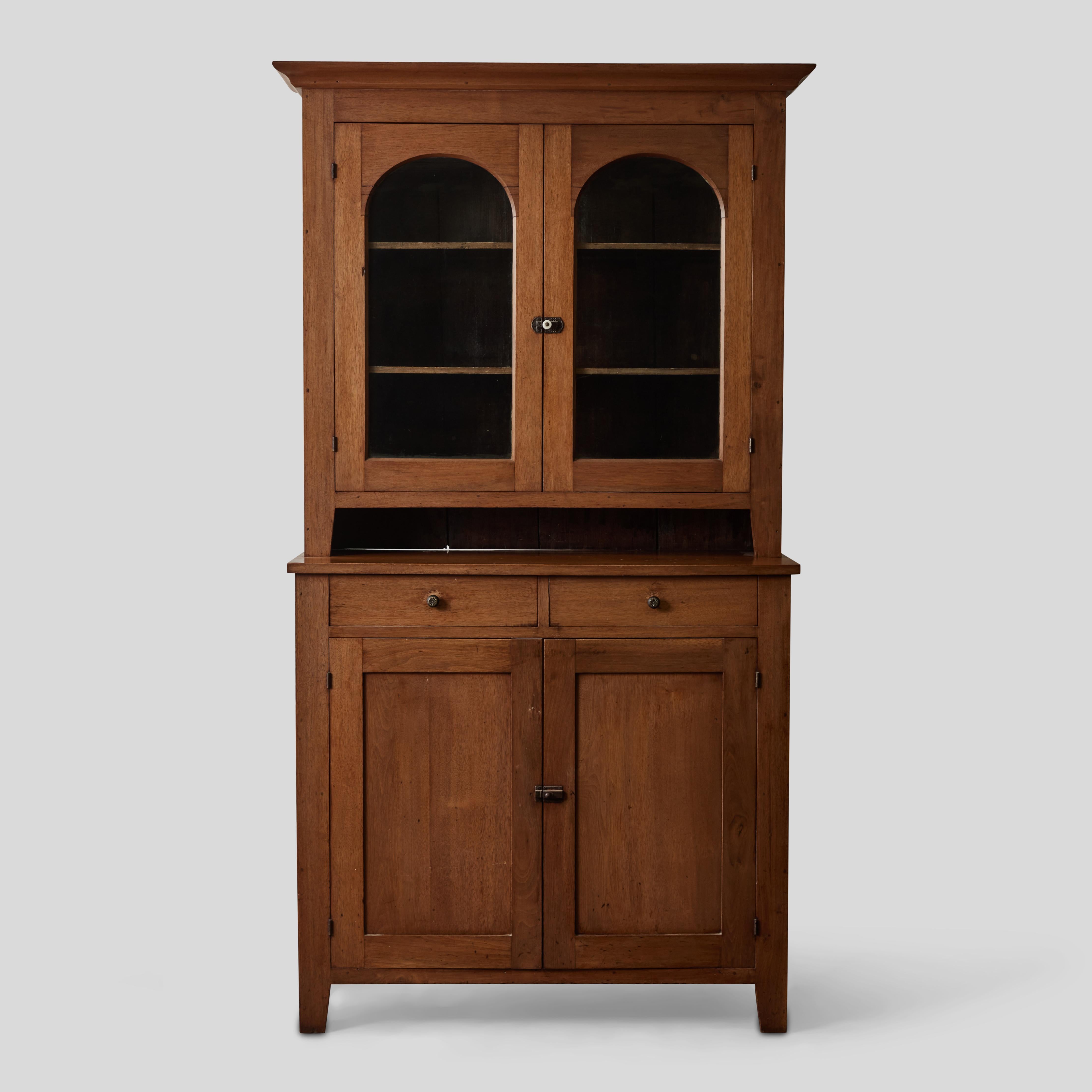 Late 19th-century Craftsman-style hutch or bookcase in mahogany. The upper section features a simple molded cornice, two adjustable shelves, and two cabinet doors inset with dome-shaped windows. The lower section is mounted on tapered block feet,