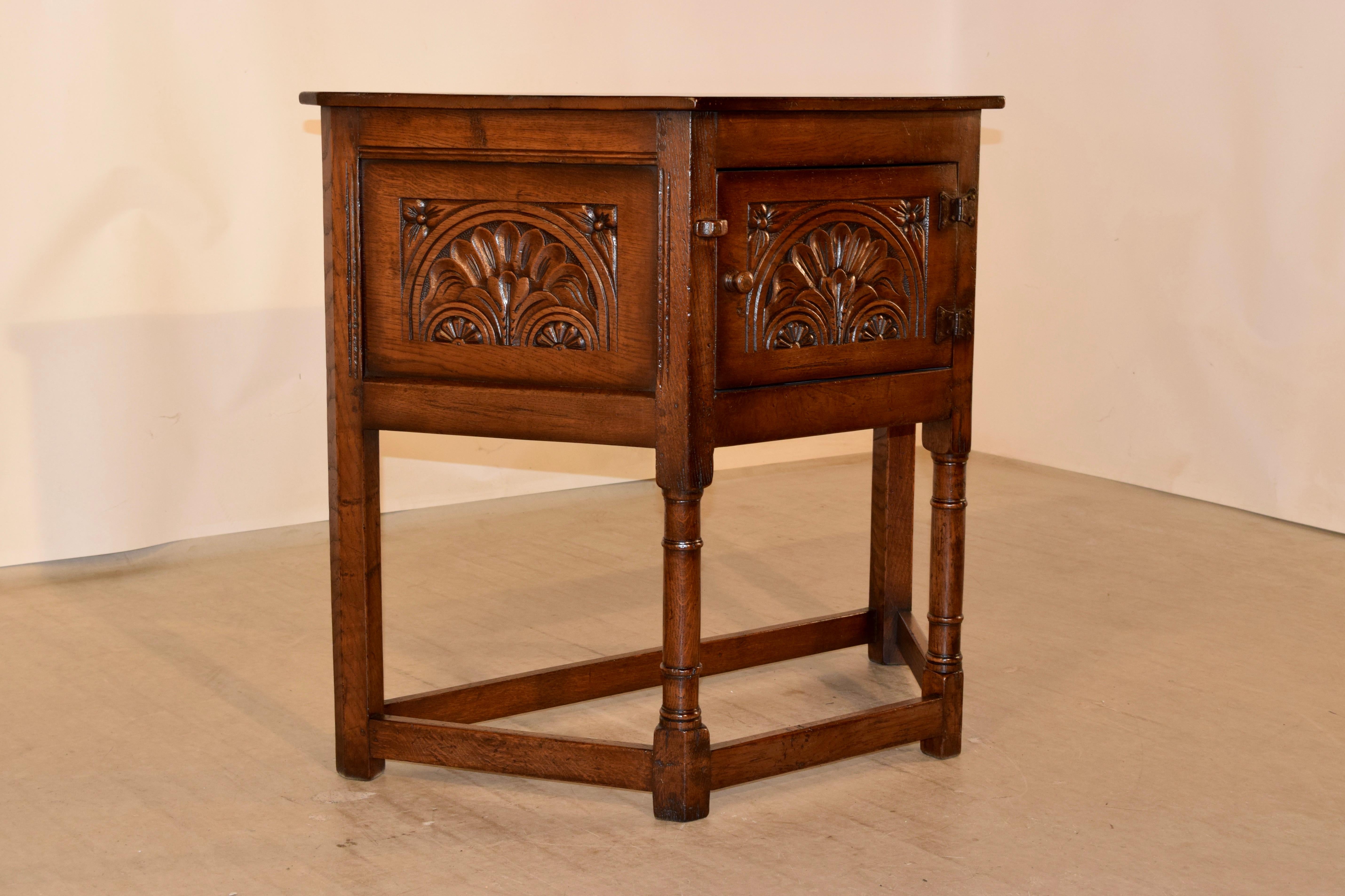 19th century English oak console table with a five-sided top following down to paneled sides with hand carved decorations and a single carved door with handmade hinges which opens to reveal storage. The piece is supported on hand turned legs, joined
