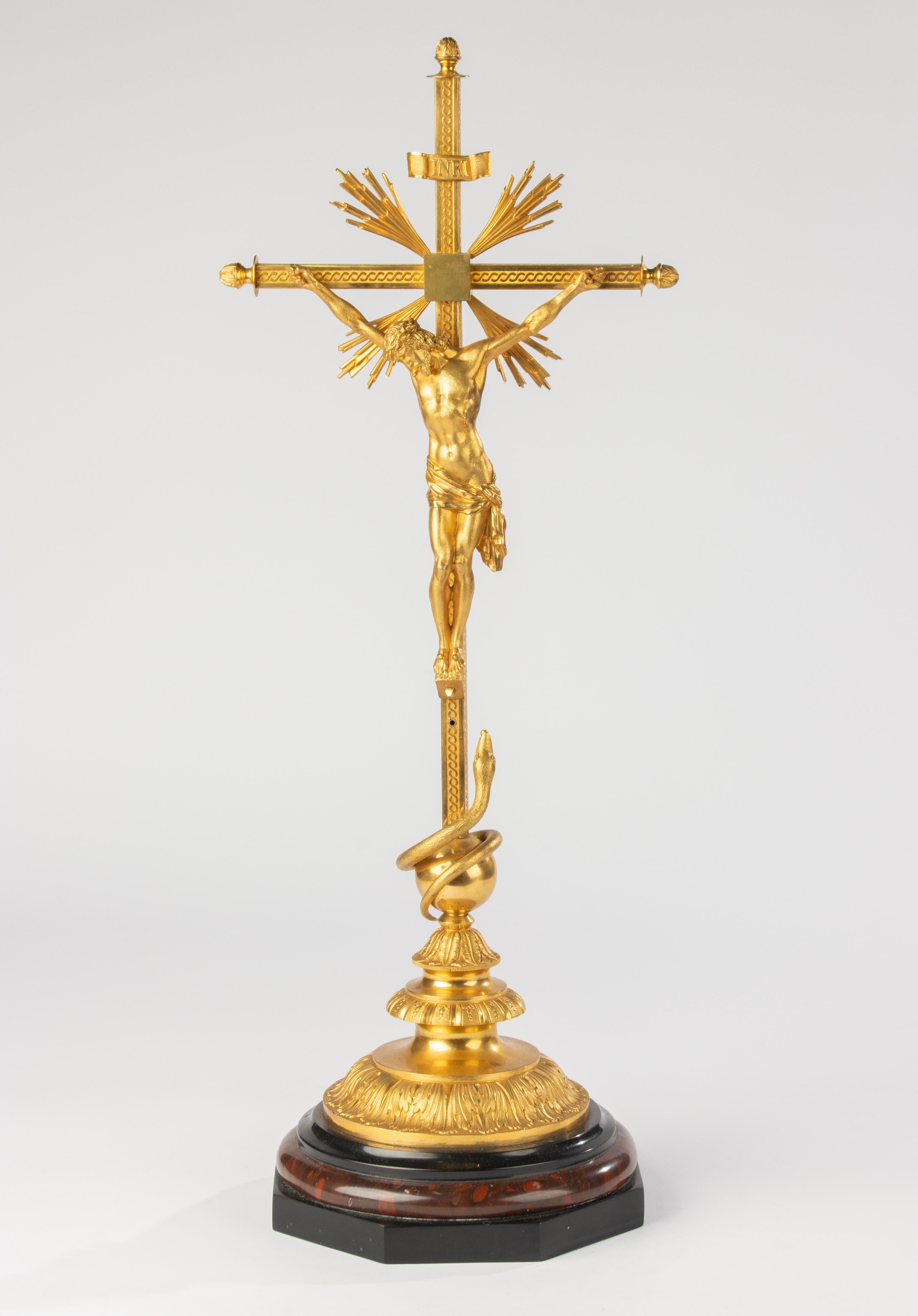 This refined French Napoleon III–style crucifix is crafted in richly gilt bronze, displaying a magnificent glow and a beautifully aged patina. The figure of Christ is rendered with remarkable anatomical detail, set against a radiant sunburst and