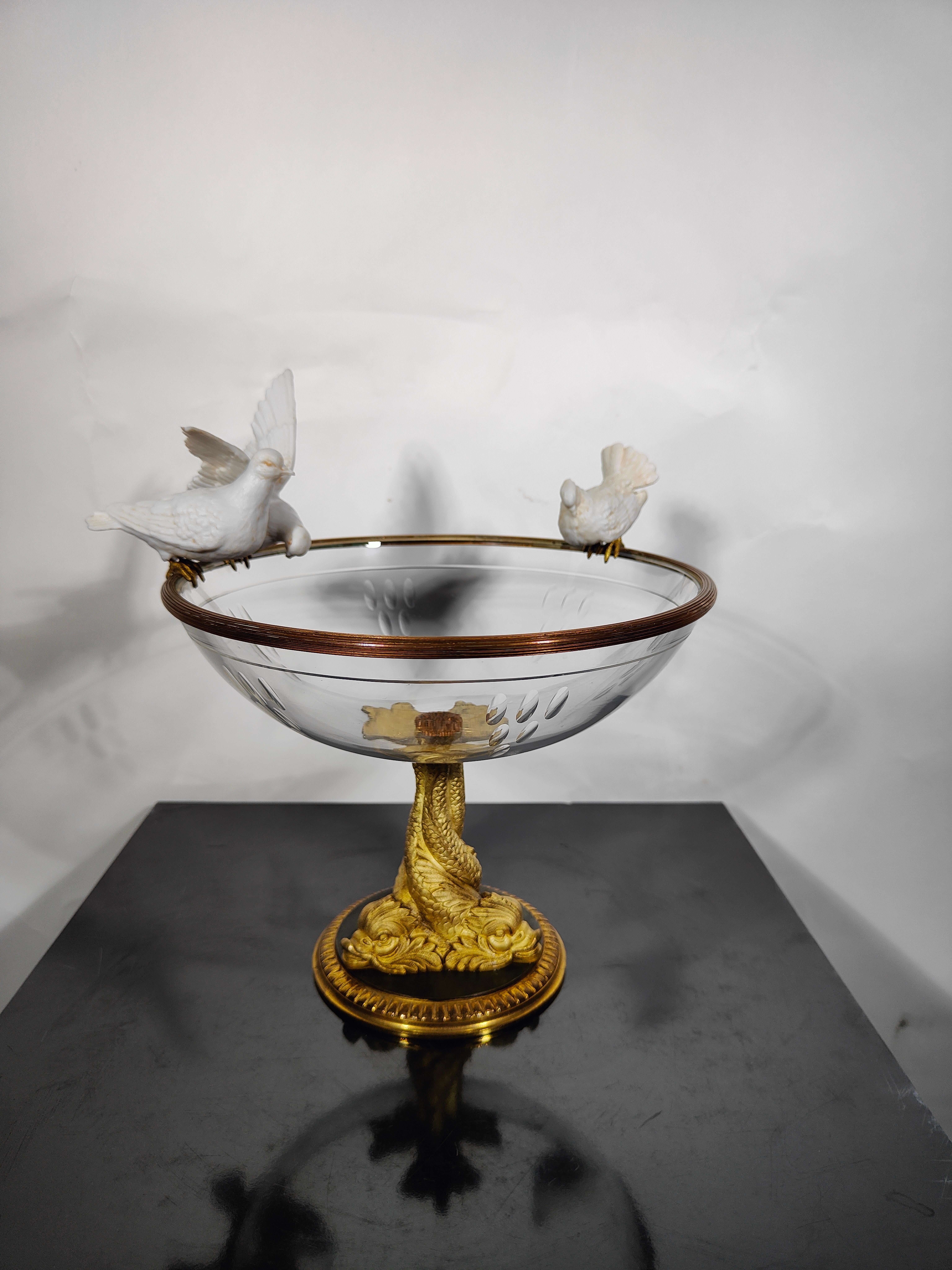 19th century Crystal and porcelain centerpiece.
19th century Crystal and porcelain centerpiece elegant centrepiece simulating a sculpted glass source where 3 porcelain birds rest supported by 3 interfaced dolphins in golden bronze. Measurements: 22