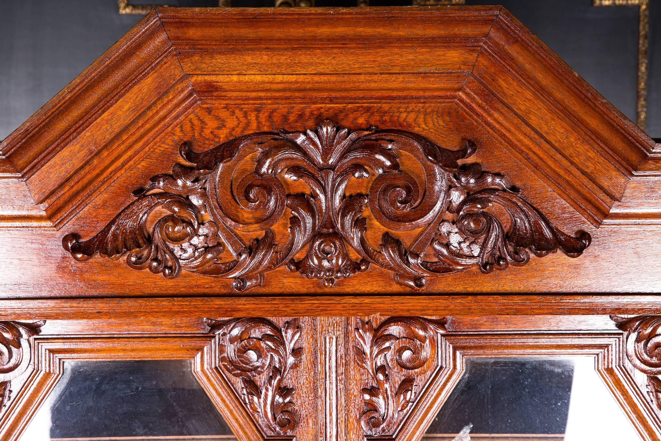 Solid oak. Chest of drawers with folding lid, as folding table, flanked by two armrests. Two-door glazed tower with carvings, flanked by turned columns. Richly carved profiled three-sided cornice.

Original furniture from the famous master carpenter