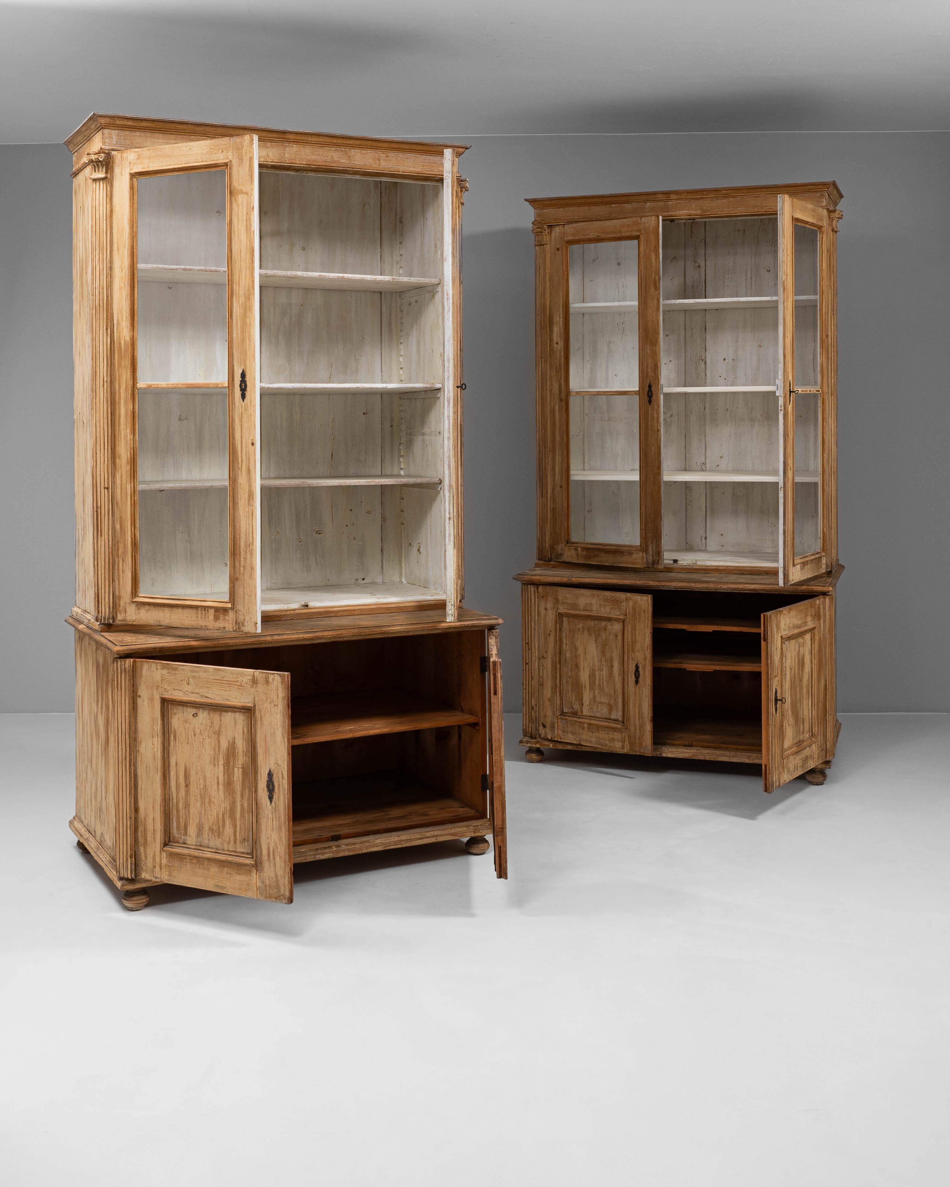 This 19th Century Czech pair of wooden vitrines combines stately presence with rustic charm. Each piece features a two-part construction: an upper display cabinet with glazed doors and painted interior shelving, and a lower storage base with paneled