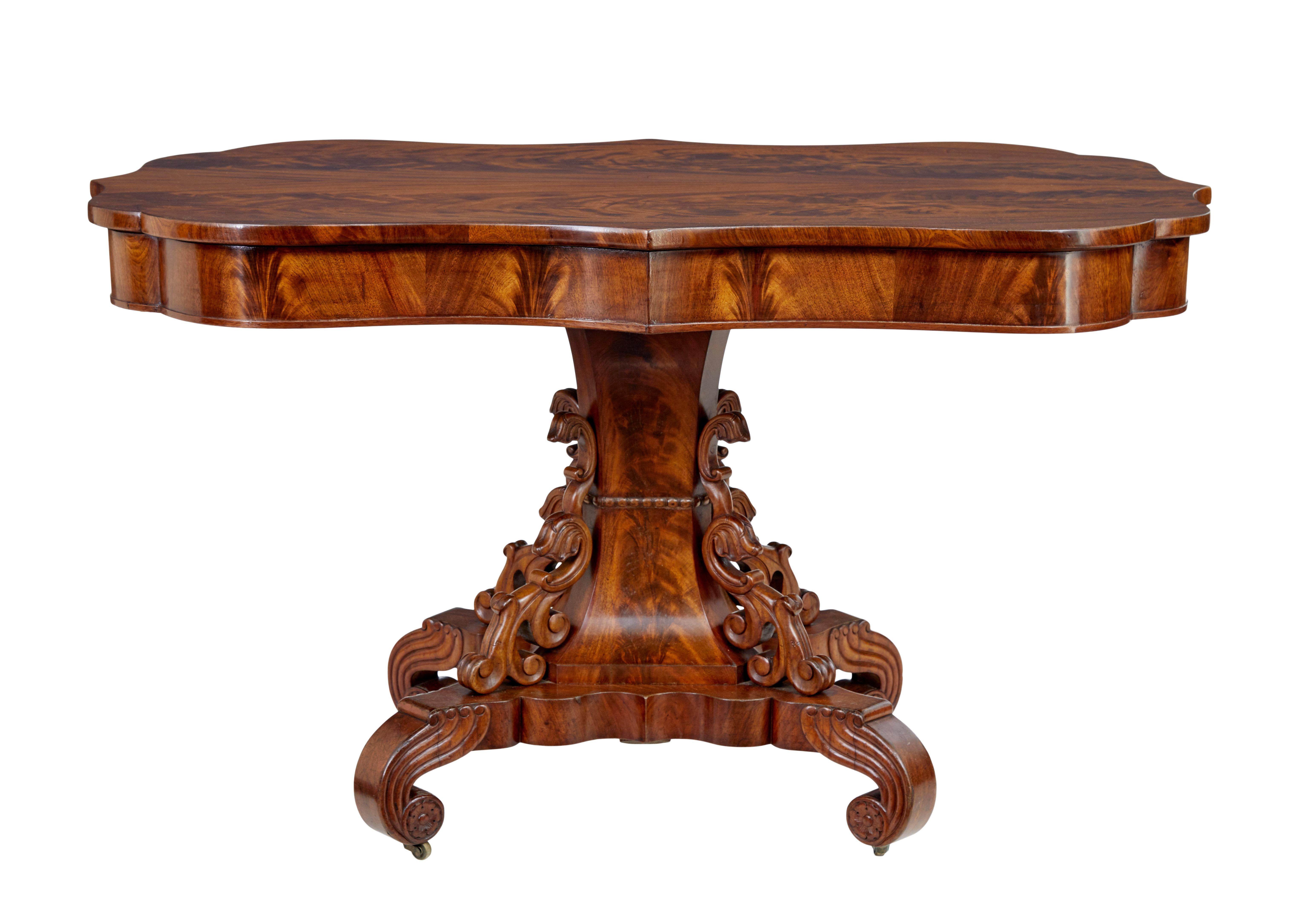 19th century Danish carved flame mahogany center table circa 1860.

Beautifully shaped top surface with striking half matching veneer top.  Slightly over-sailing top sits on an apron of the same shape.  Supported by a fluted steam which splays out