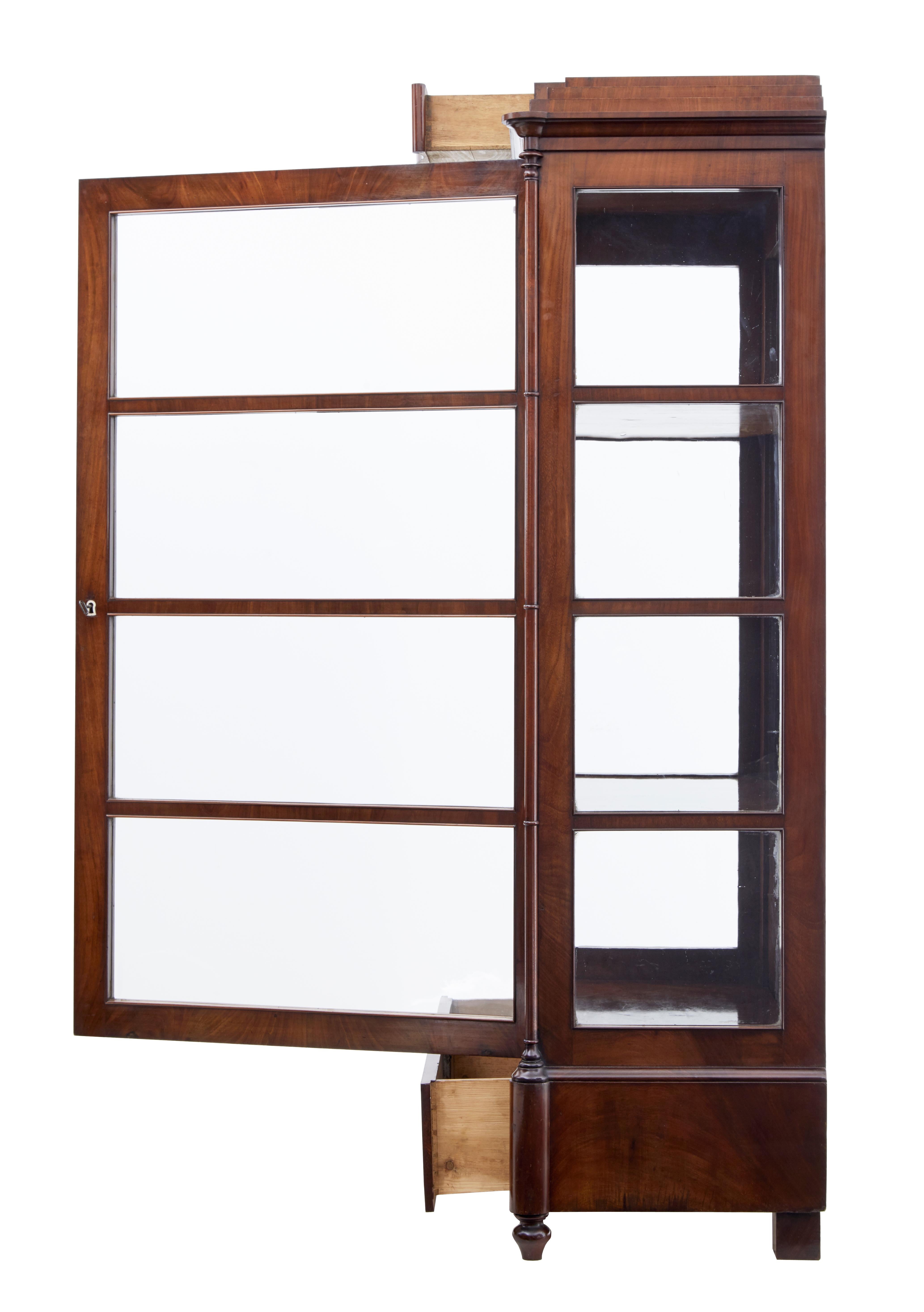 Rare Danish flame mahogany display cabinet, circa 1840.
Single door cabinet containing three mahogany shelves with original mirrored back panels.
Original glazing to the front and sides.
Concealed drawer in the pediment with a further deep drawer