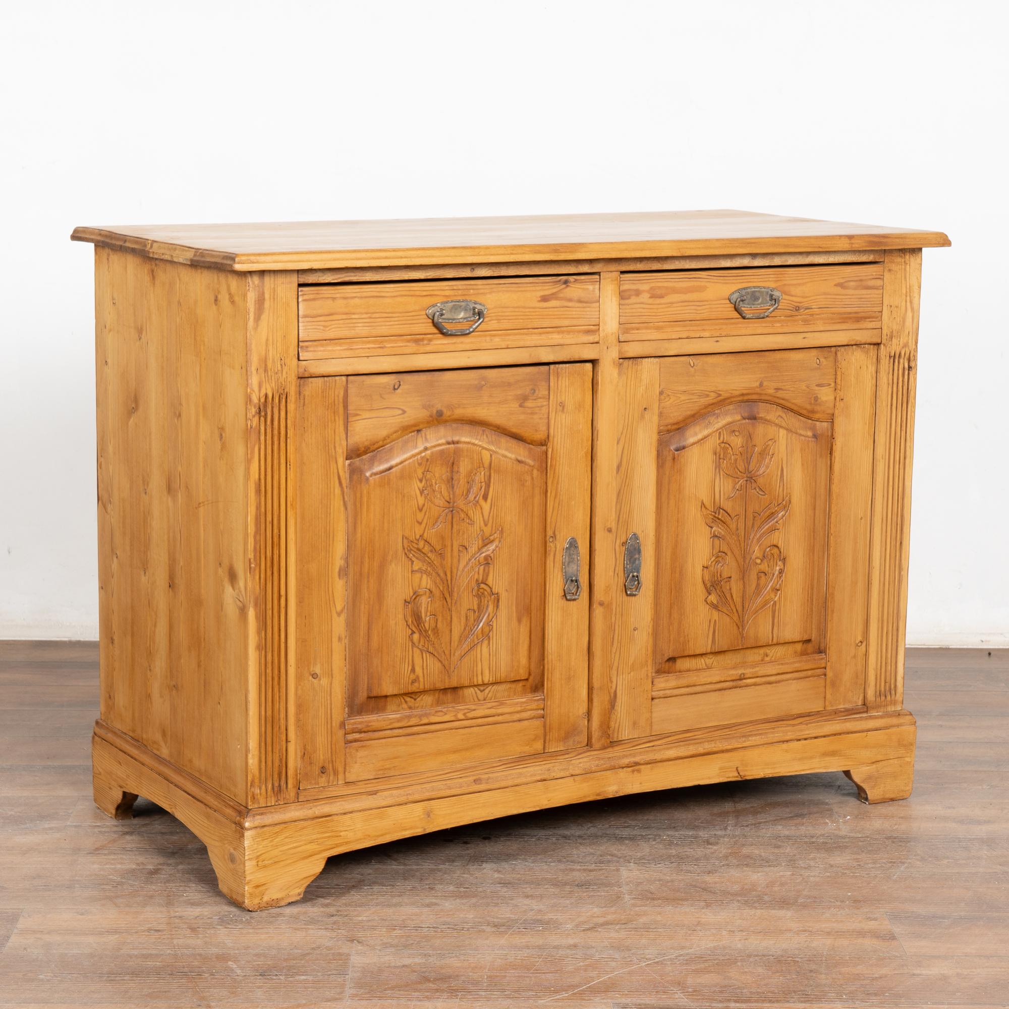 Danish pine sideboard with floral carving along front door panels. Two drawers over two doors.
Restored and waxed, this cabinet is stable, strong and ready for use. Brass pulls on each door; no lock, snap closure. Drawers function.
All scratches,