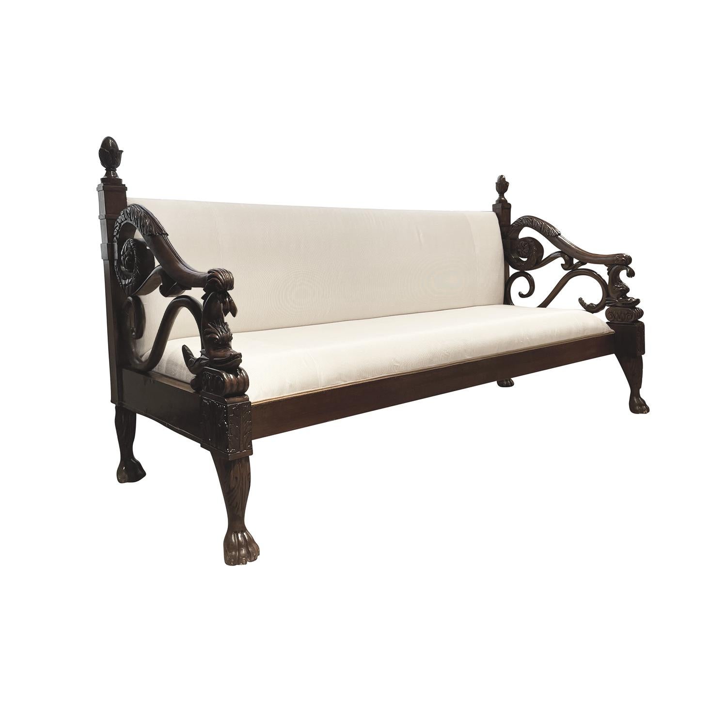A dark-brown, antique Baltic long bench with two pillows made of hand carved Mahogany, in good condition. The three seater sofa, settee is standing on four paw feet with pinecones as pinnacles and elaborately carved armrests in the form of dolphins