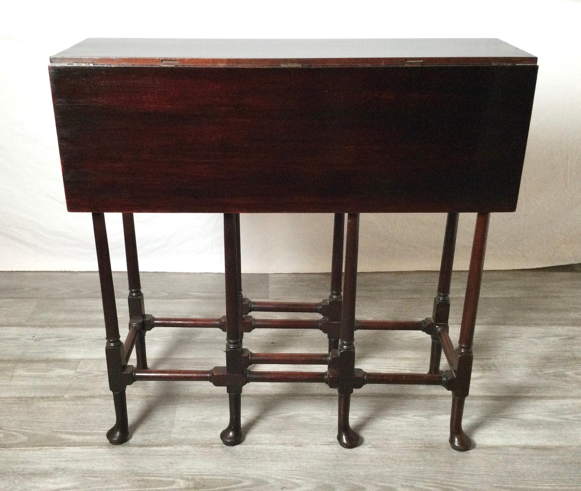 Charming dark mahogany gateleg table. The turned legs with spoon feet having two that swing out to support each of the side leaves. The slim profile of 9 inches with additional 9 inch leaves on each side.