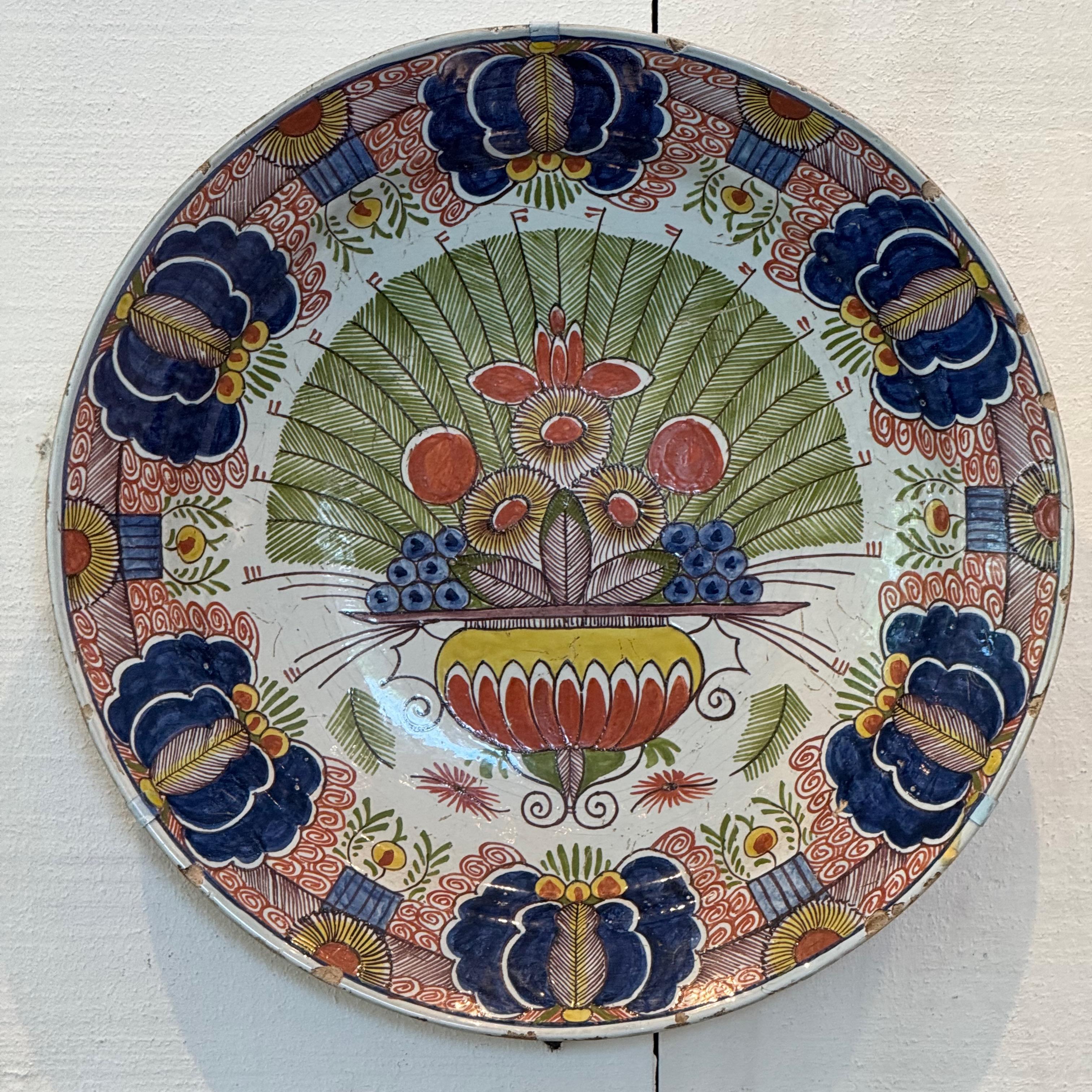 Gran bandeja de Delft pintada a mano, hacia 1840, con un arreglo floral central en una urna estilizada con motivos de hojas radiantes y un atrevido borde de flores de color cobalto y óxido. Vívidamente coloreada con esmaltes policromos