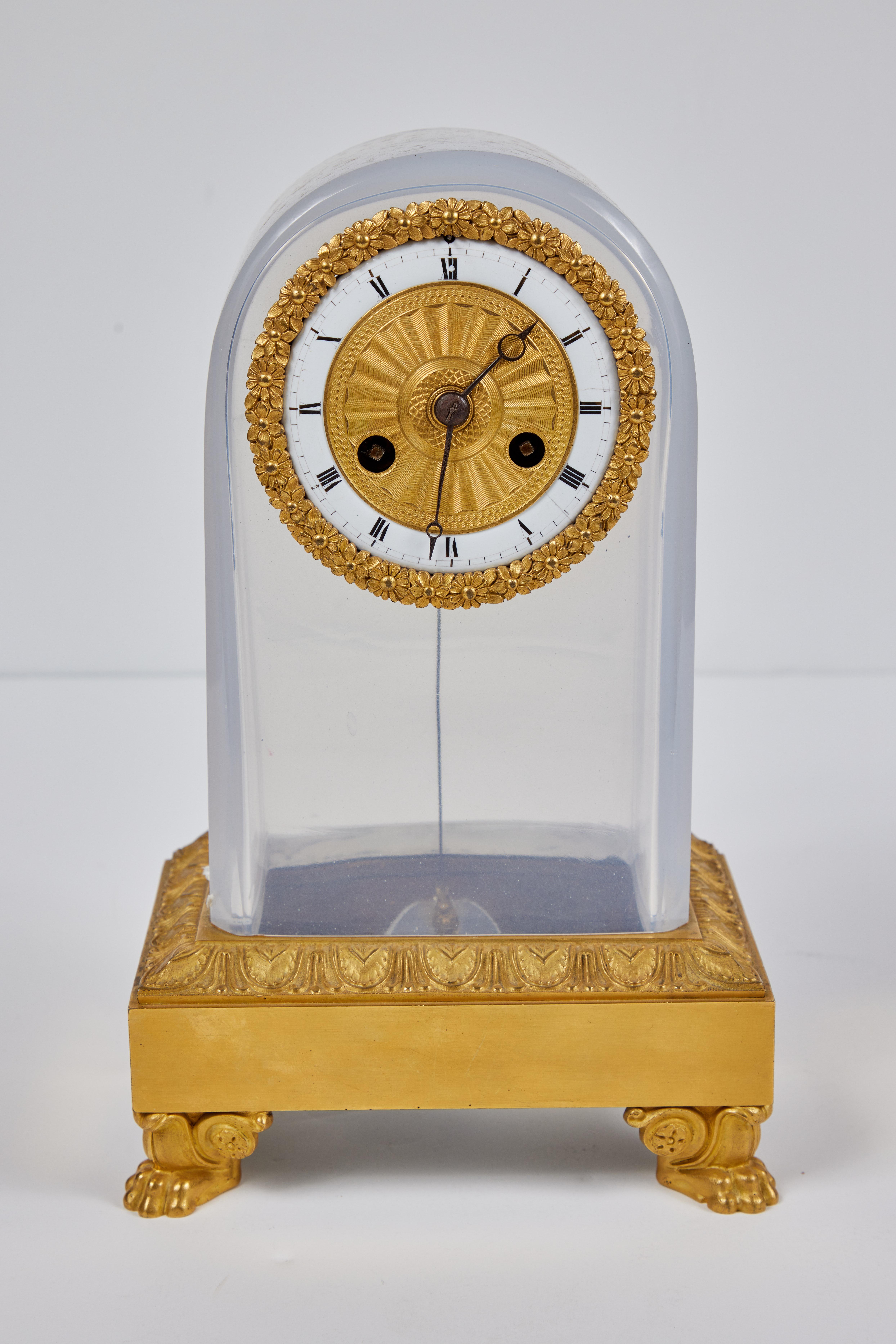 A chic, c. 1825 French, looping desk clock with a central timepiece framed in foliate embellished, bronze doré wreath. The clock set into a pale blue, Opaline glass casing atop a gilt bronze base that sits on four, paw feet.