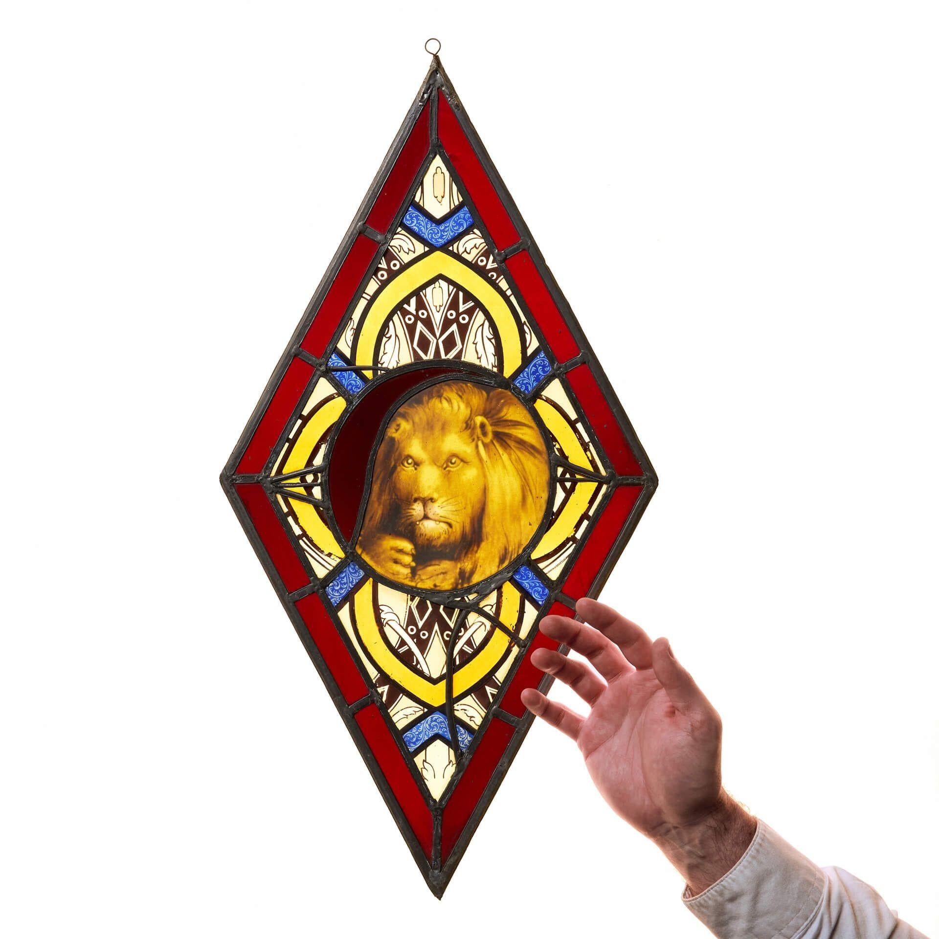 A small 19th century lozenge or diamond-shaped stained glass panel, centred with a lion portrait. This striking stained glass window hanging is striking and vibrant, the lion surrounded by blue and yellow glass within a red stained glass frame.