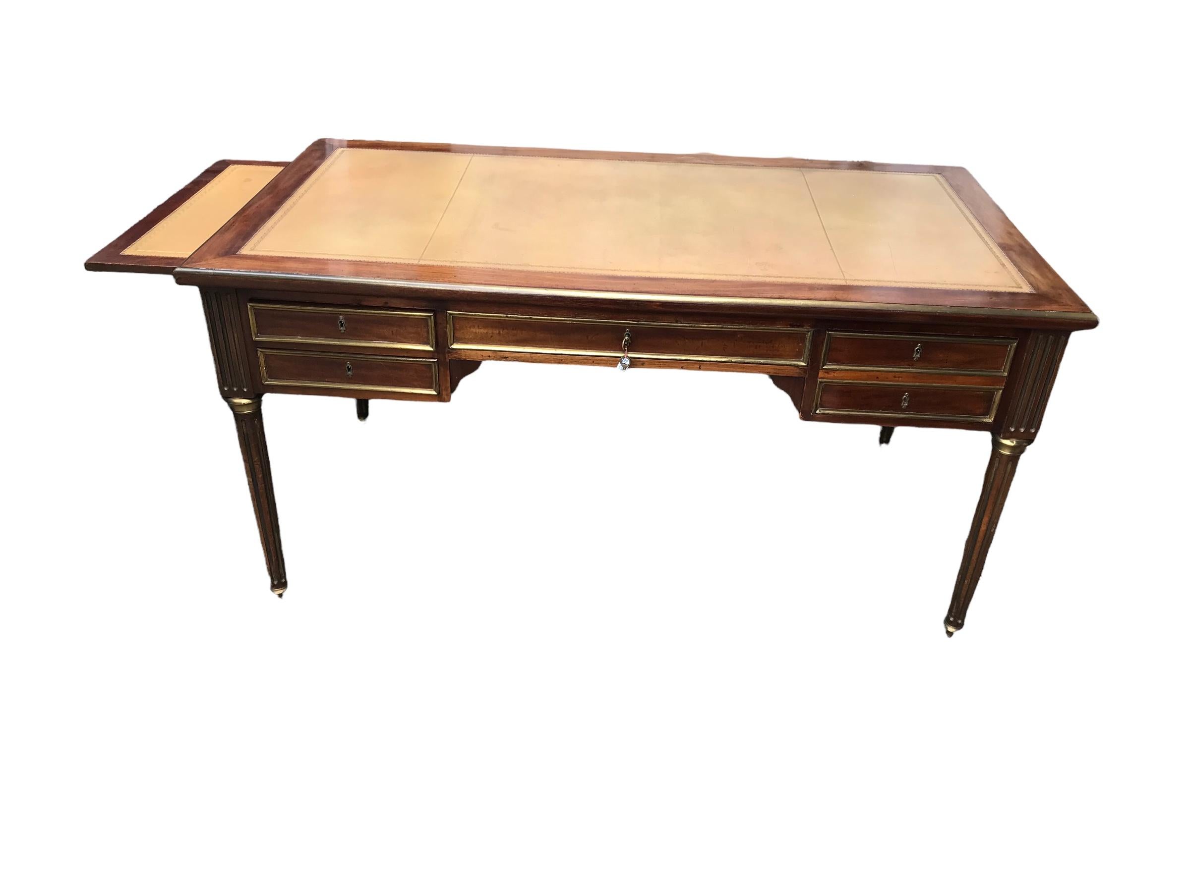 This elegant Directoire style desk dates back to the second half of the 19th century. The desk has a pretty mahogany veneer and is additionally embellished with brass fillets. The top is covered with light brown leather and has two additional