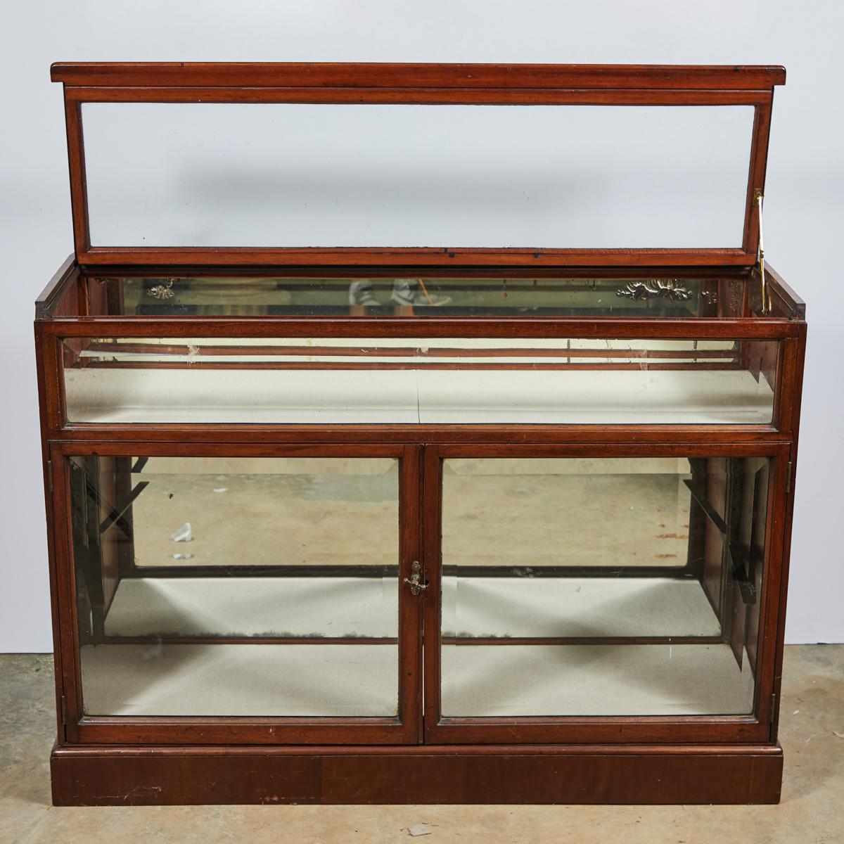 English 19th-century glass display case with mahogany framework and mirrored back panelling. The two main compartments--an upper shelf tray and a lower cabinet display--make great opportunities for the presentation of a collection.

England, circa