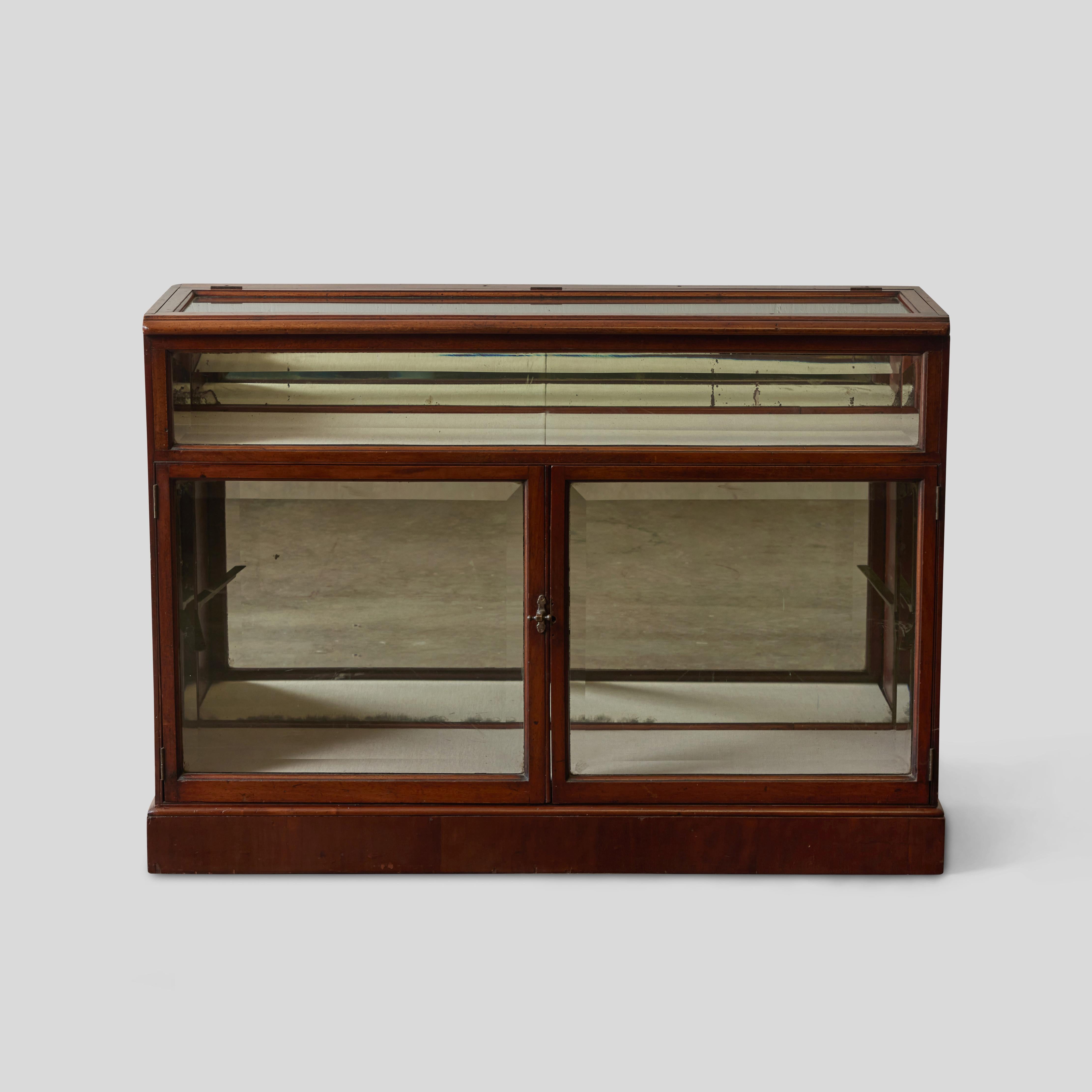 English 19th century glass rectangular display case with mahogany framework and mirrored back panelling. The two main compartments--an upper shelf tray and a lower cabinet display--make great opportunities for the presentation of a collection.