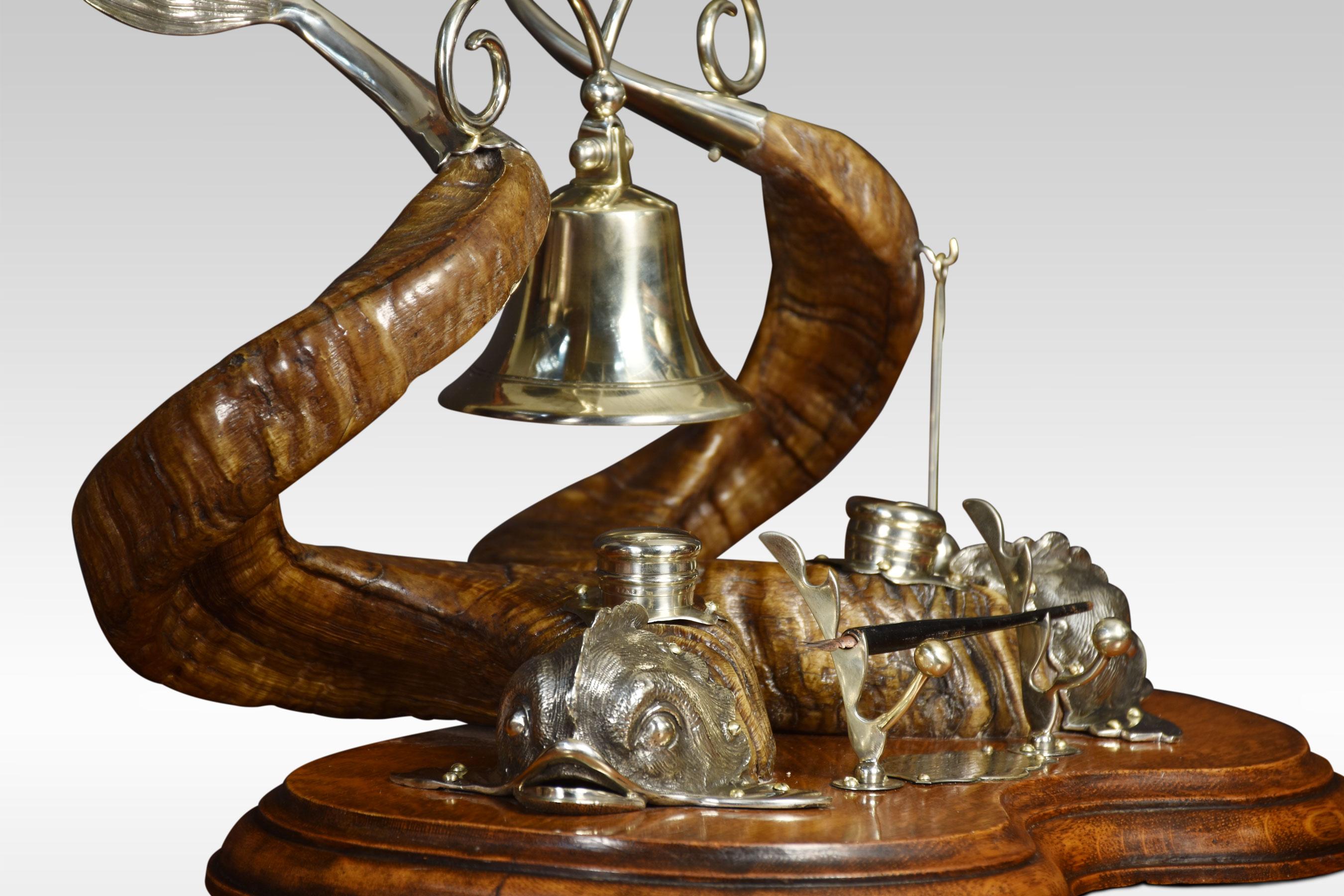 Ram horn and silver plate dolphin inkwell, bearing a pair of ram’s horns, mounted with plated dolphin mounts, the tail suspending a bell, the beater for which is on mounts to the front near the pen well. All raised up on oak base
Dimensions
Height