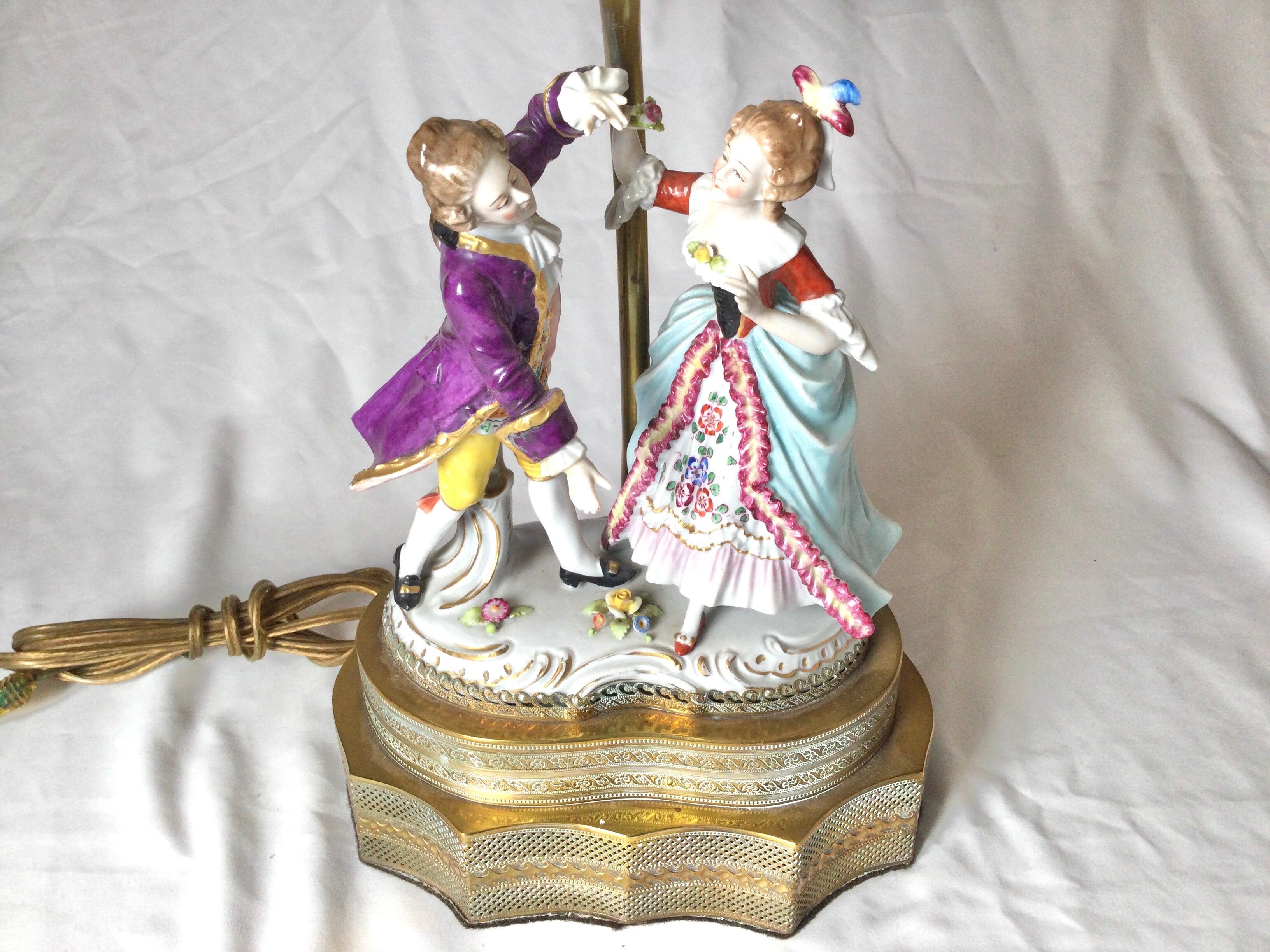 A finely painted Dresden porcelain figurine from the 19th century now as a lamp. The figure of a 18th century style courting couple that has not been drilled. The aged brass base and pole which was added in the earlier part of the 20th century. The
