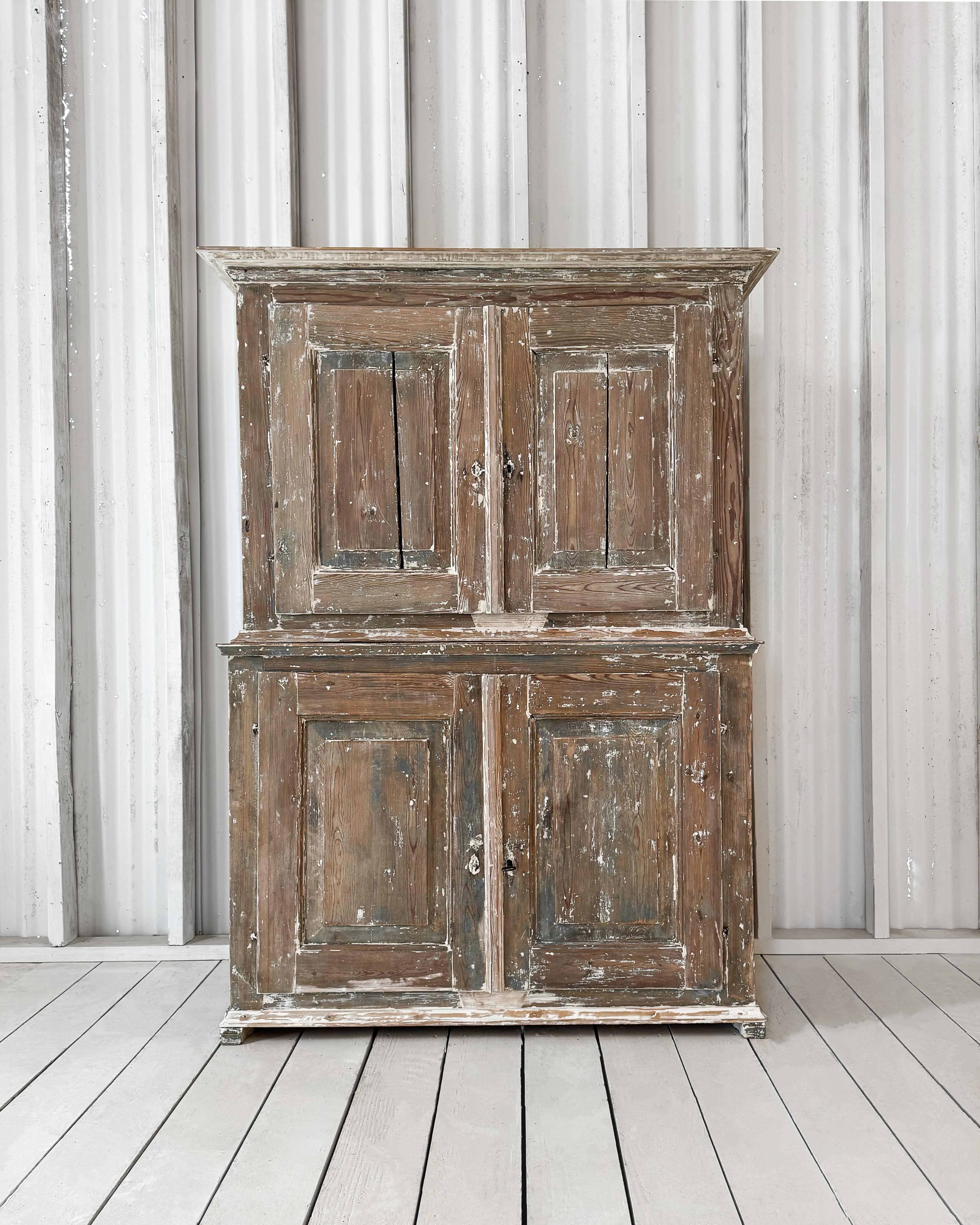 Composta da un pezzo superiore e uno inferiore, questa bella credenza a 4 ante vanta una finitura unica. Strati di vernice grigio-blu e bianco crema sono stati meticolosamente raschiati a secco per rivelare il legno naturale sottostante, lasciandone