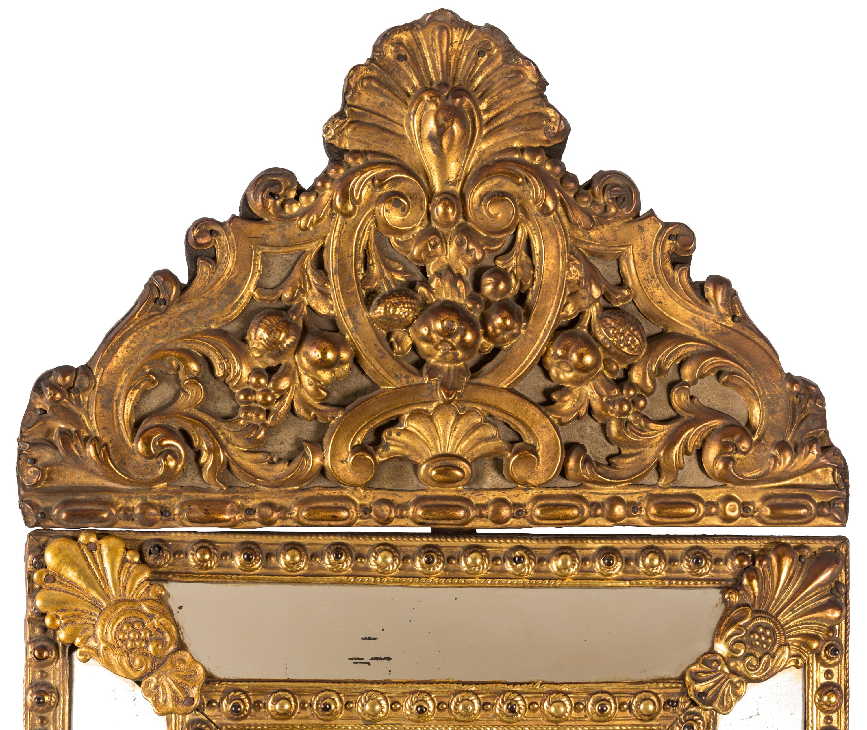 A 19th century Dutch Baroque style mirror with beveled central glass and gold colored metal frame with embossed, sculptural decoration. The raised designs were handcrafted using a technique known as “Repoussé” in which the metal (in this case either