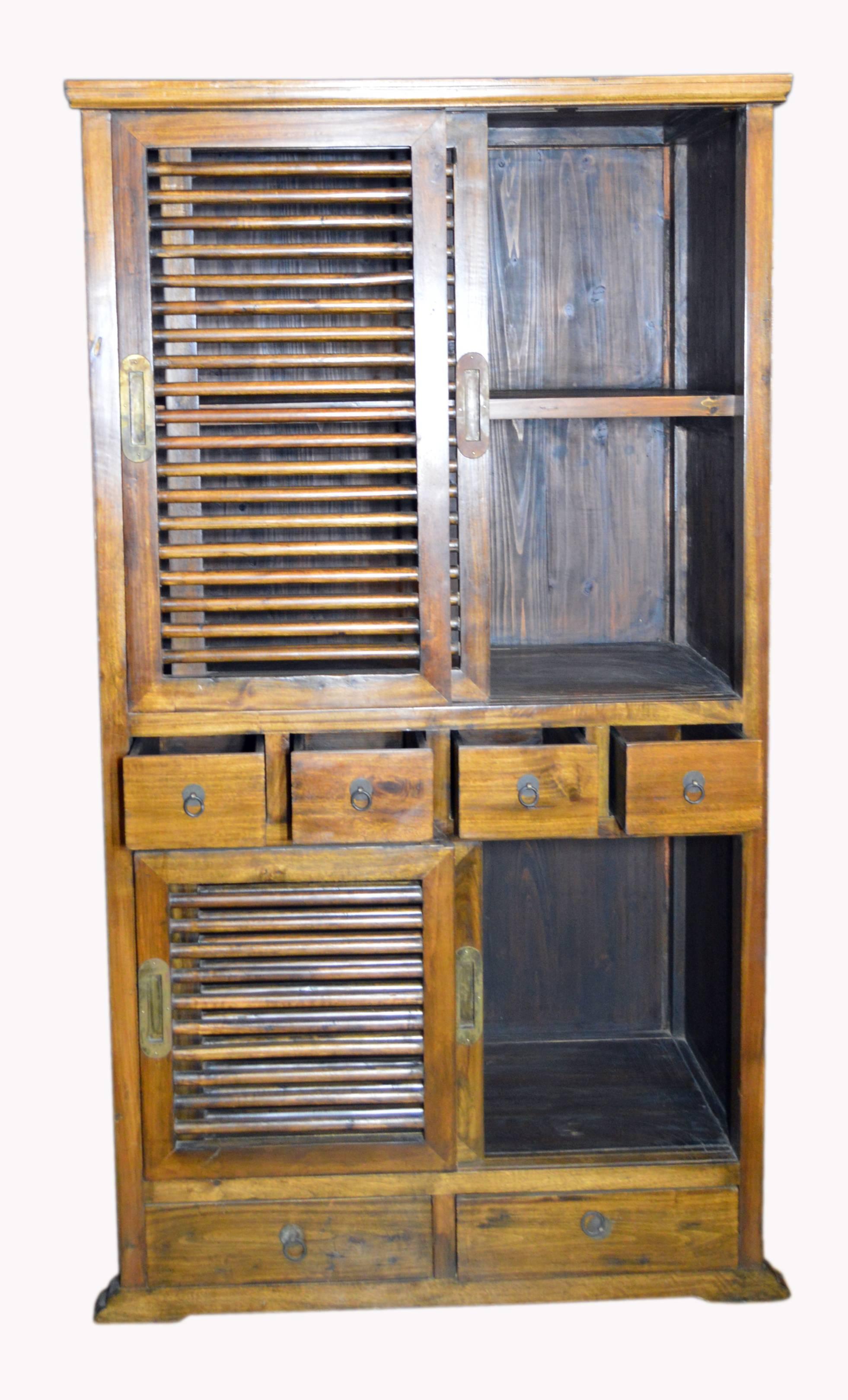 A tall 19th century Dutch Colonial Indonesian armoire with sliding doors, drawers, brass handles and natural patina. This unusual Dutch Colonial armoire features a thin molded cornice sitting above two fretwork sliding doors with brass handles.