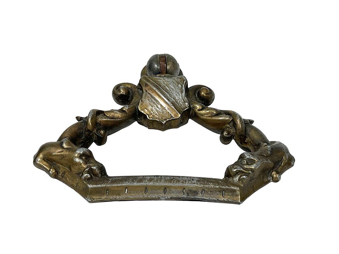 19th Century Dutch Door Knocker

A heavy door knocker with a coat of arms on top in between scrolls, with a dragon twisting around the handle to the right and left. The knocker is checked with a magnet, it is not magnetic, so it is not metal or