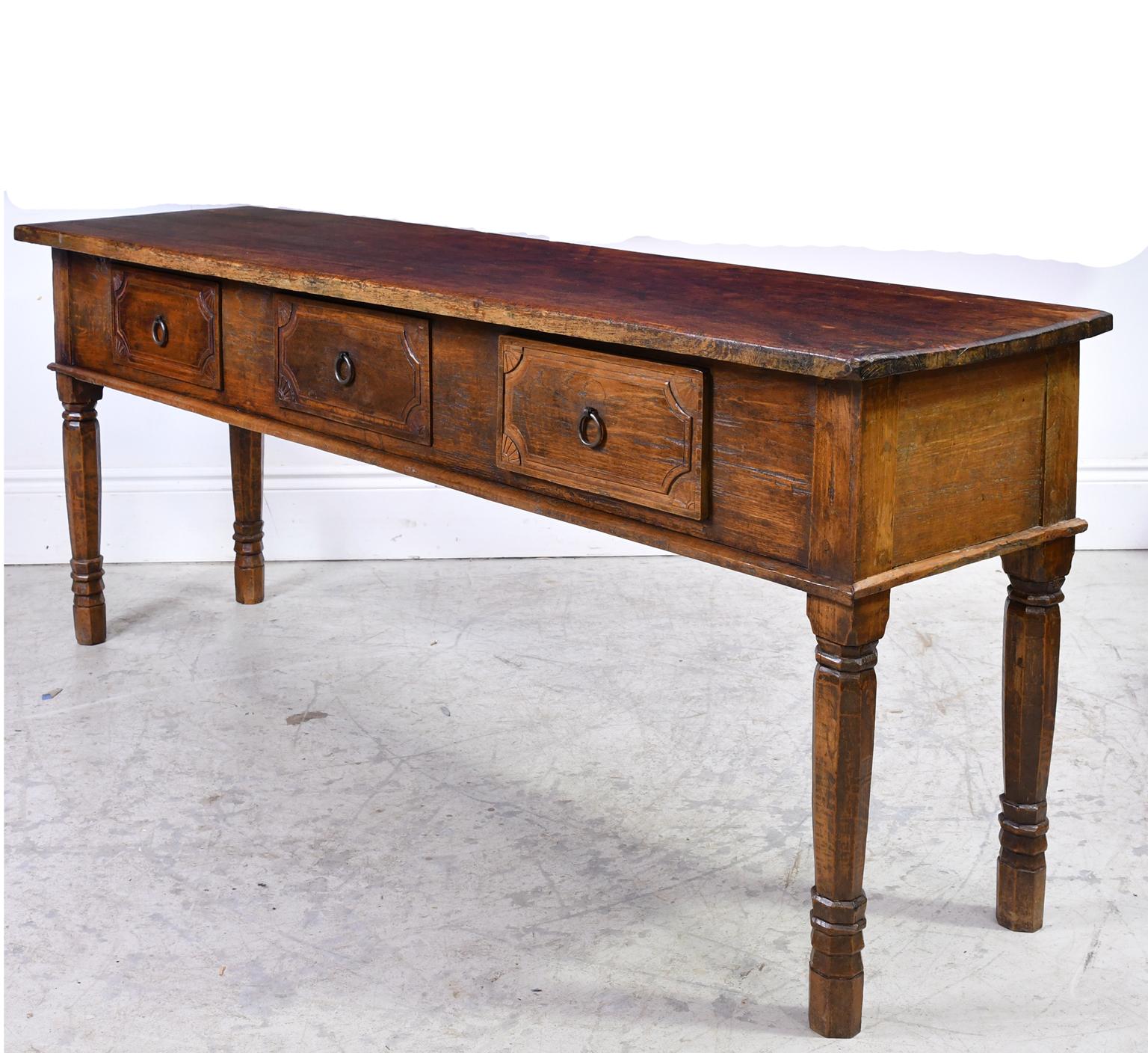 From the East Indies, a farmhouse table in teak wood with plank-top, turned legs and offering three drawers with carved fronts and original ring pulls. Indonesia, circa mid-1800s.
Measurements: 74 1/2