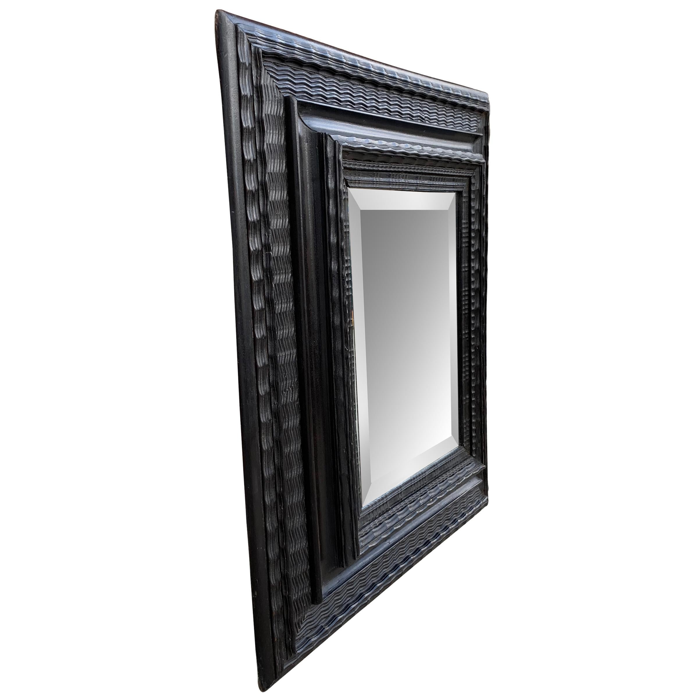 A beautiful 19th century Dutch ebonized frame with a wide profile containing multiple carved patterns framing a newer beveled glass mirror. An iron ring on the back can orient the frame vertically or horizontally.