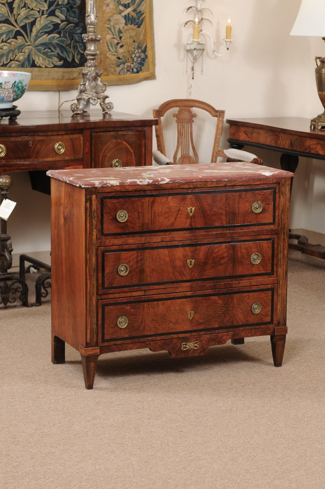 A 19th Century Dutch Neoclassical Walnut Commode with unique Red Marble Top. Striking woodgrain and inlay on each of its three drawers. This piece features brass ring pulls, brass faux keyhole mounts and a decorative apron with tapered front legs.