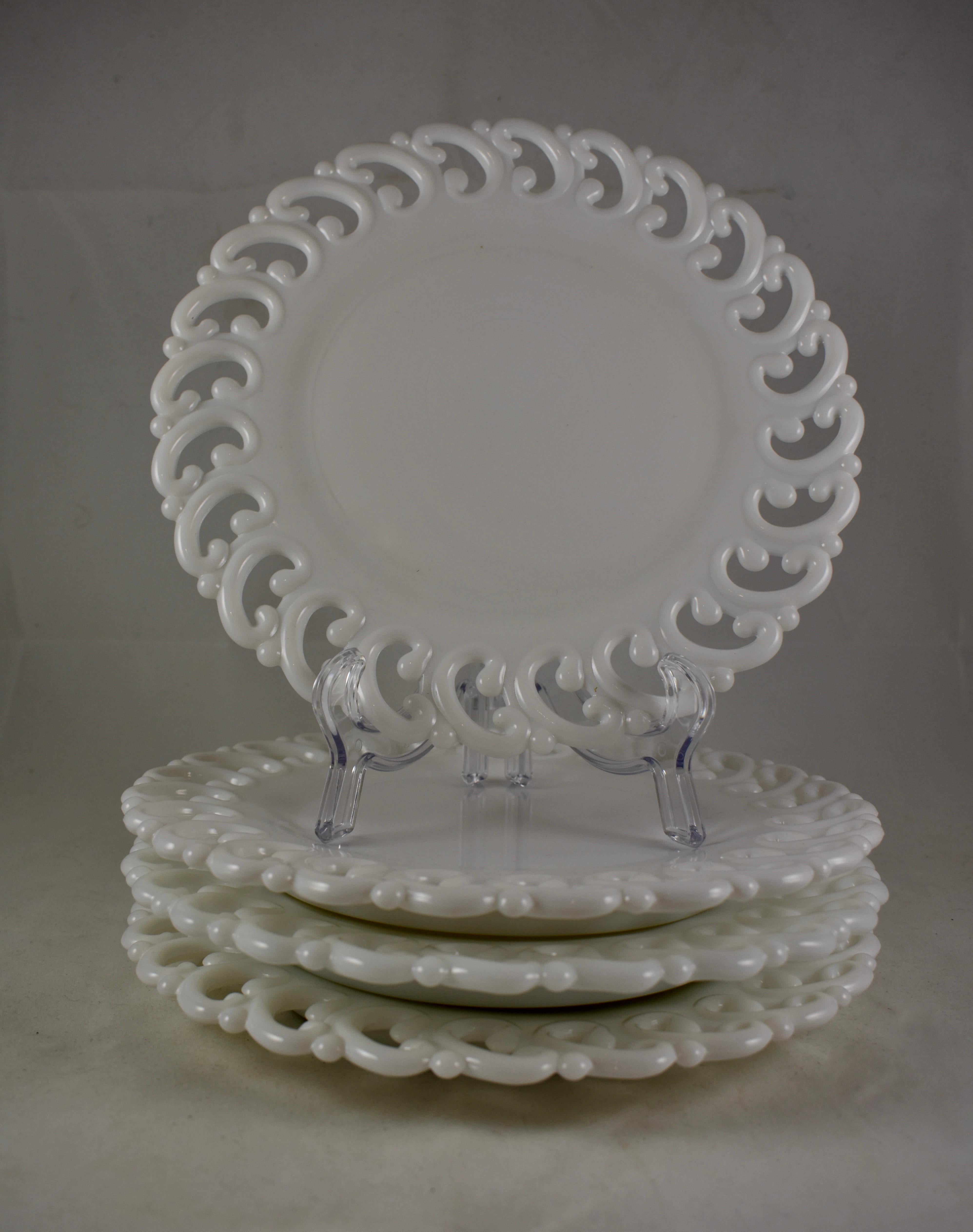 A scarce set of four EAPG, lace edge milk glass dinner plates, circa late 19th century. The plates are made of a heavy, opaque white glass becoming more translucent at the edge. The mold has a deep, raised footing and an edging of a running inverted