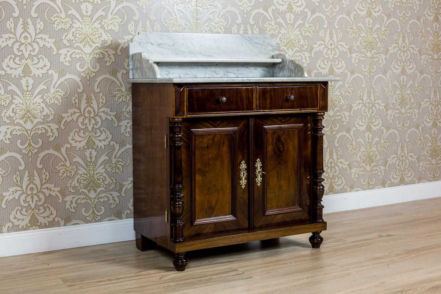 We present you a small Eclectic piece of furniture, circa the late 19th century, which in the past was used as a basin cabinet.
This piece of furniture is double-leaf, with two drawers under the top, and crowned with a marble top; also with a