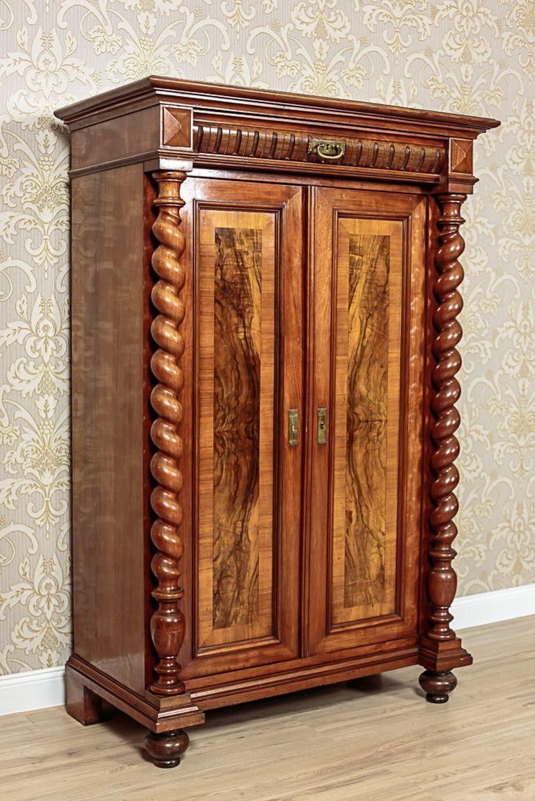 A piece of furniture in the Eclectic style from the second half of of the 19th century.
The leaves of the doors have been seized between spiral columns that support a narrow drawer above them.
The door panels are decorated with a veneer, which has