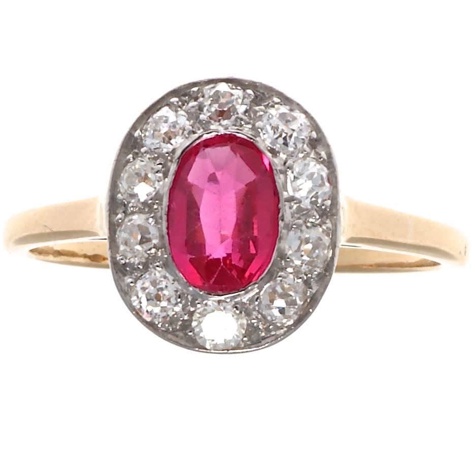 One oval faceted synthetic ruby weighing approximately 0.75 carats is illuminated by a halo of 10 old European cut diamonds weighing approximately 1.00 carat, all set in platinum. The delicate setting sits atop an 18k yellow gold open gallery. Size