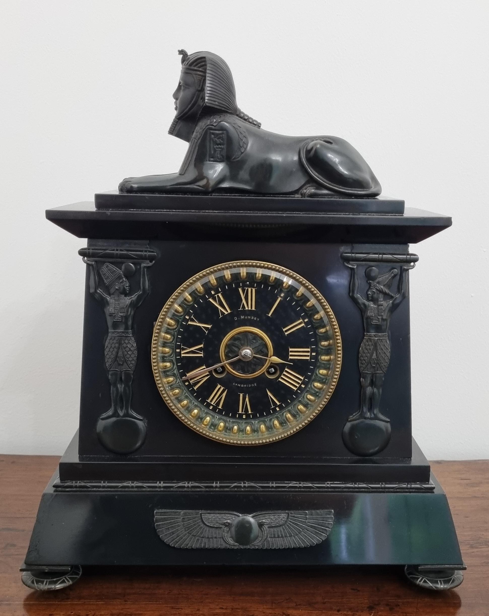 Fino reloj de chimenea de renacimiento egipcio vendido por D. Munsey de Cambridge, hacia 1880, caja de mármol negro y pizarra con elaboradas monturas de bronce.

La caja arquitectónica está coronada por una esfinge de bronce finamente fundida.