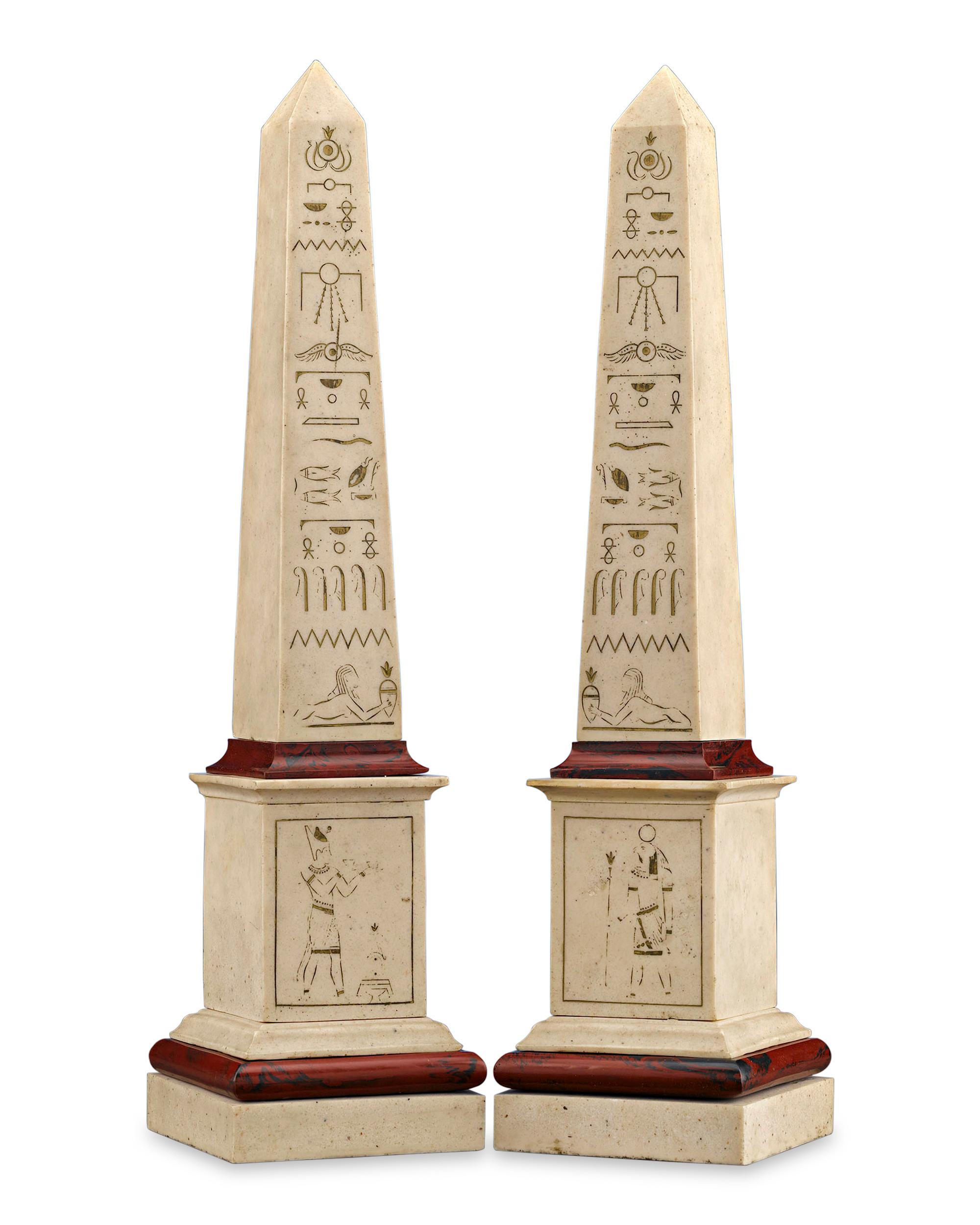 This extraordinary pair of Egyptian Revival obelisks are elegantly crafted of composition stone and faux marble. The rare 19th century models are adorned by intricately hand-carved hieroglyphics that extend upwards on their proportionate forms,
