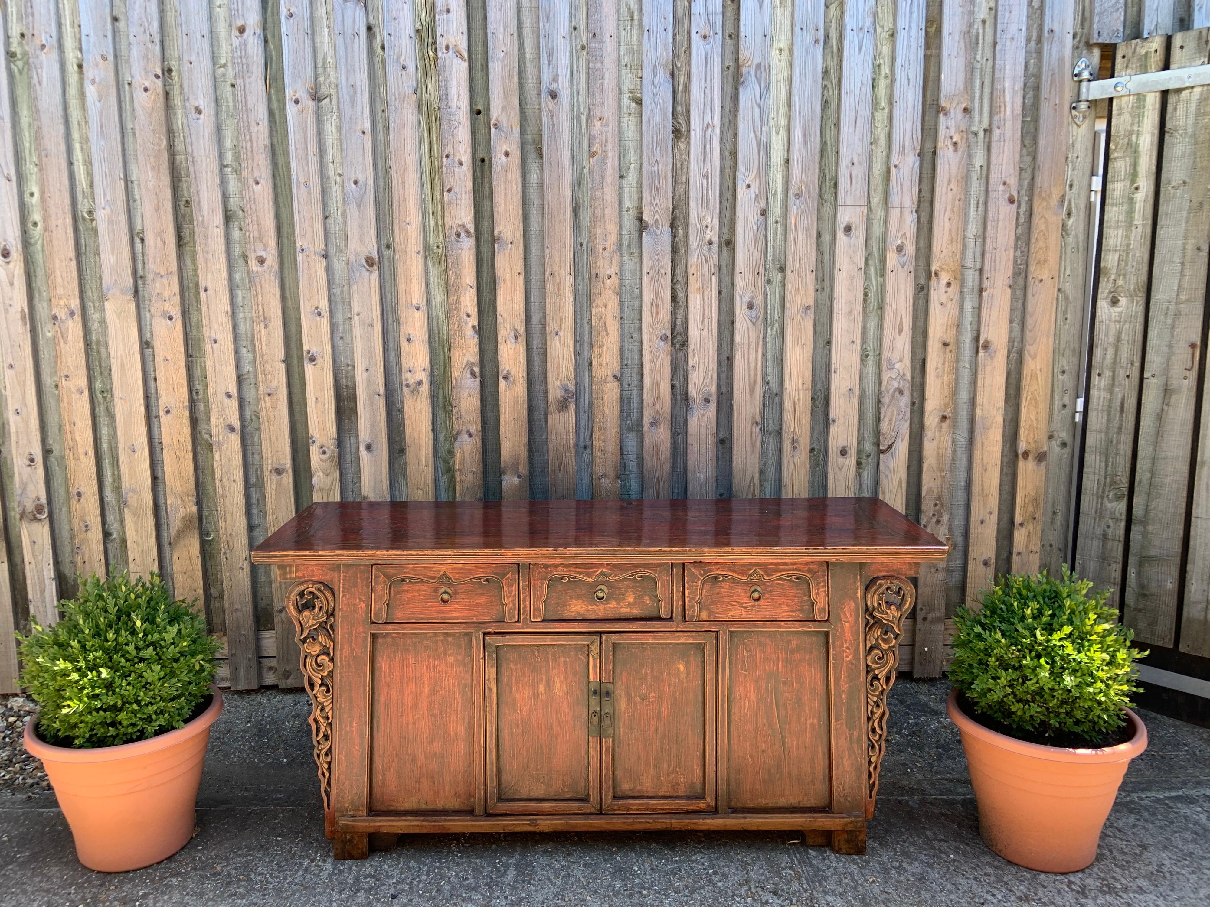 Mid-19th century elm Chinese sideboard finished in clear matte lacquer over reddish brown well patinated original color. The framed panel construction has relief dragon carving spandrels. The centre doors have wooden peg hinges that can be removed.